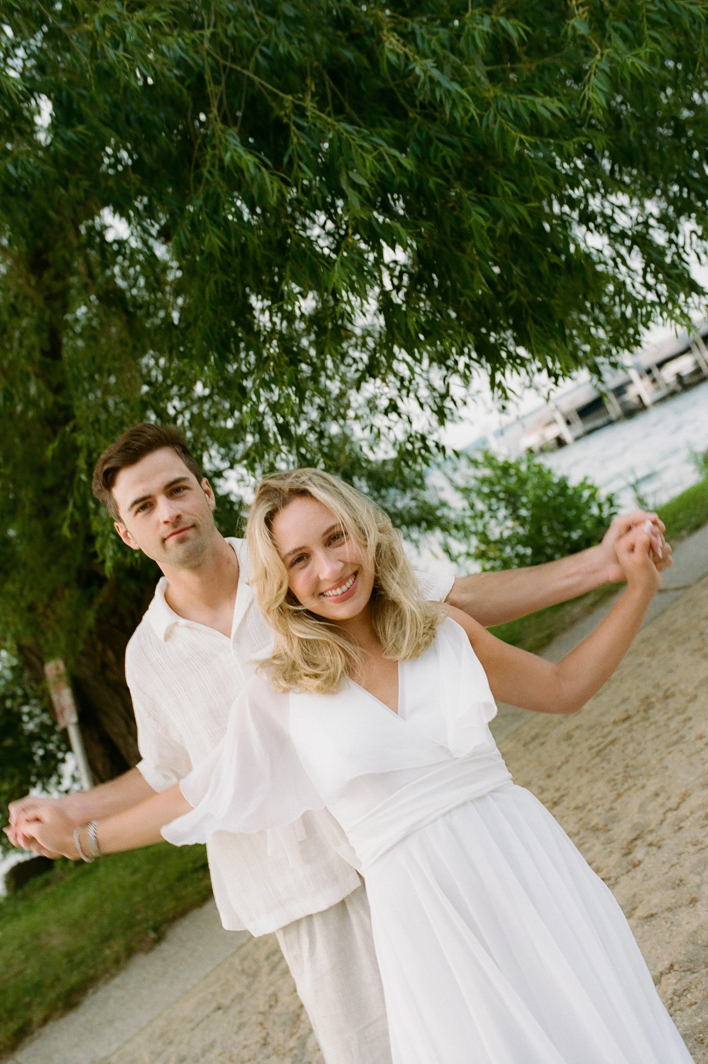 Joyful engaged couple smiling together beneath a large tree along the Lake Geneva shoreline.