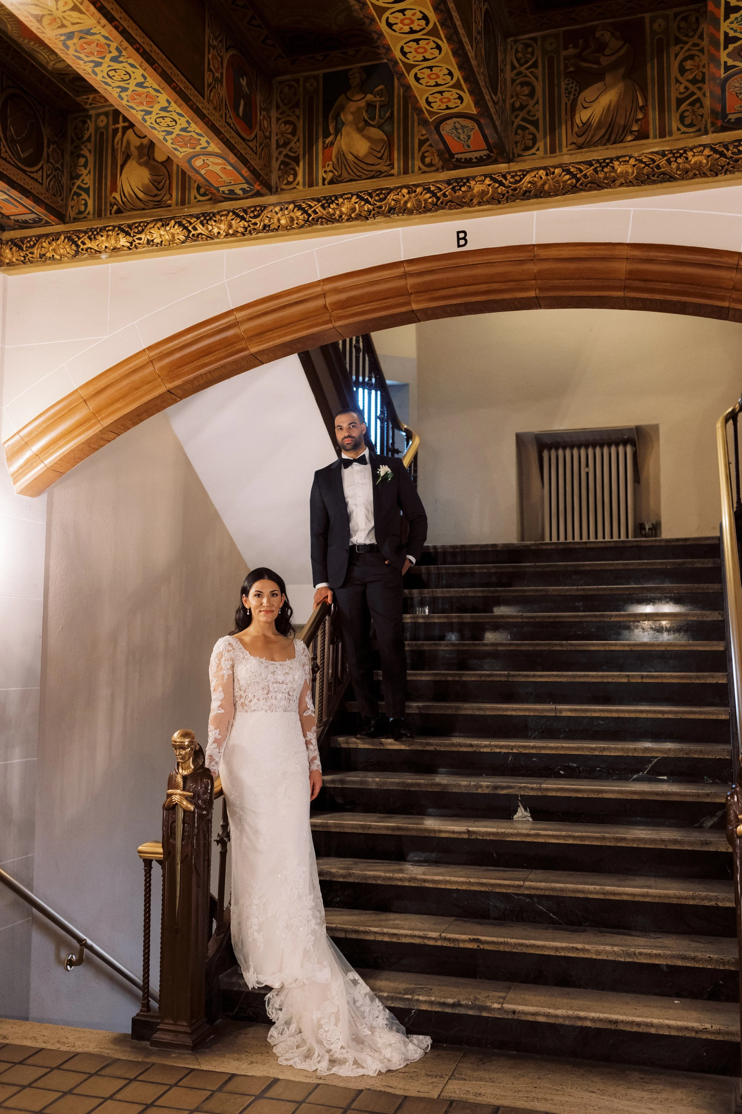 Bride and groom posing on an ornate historic staircase in their formal wedding attire.