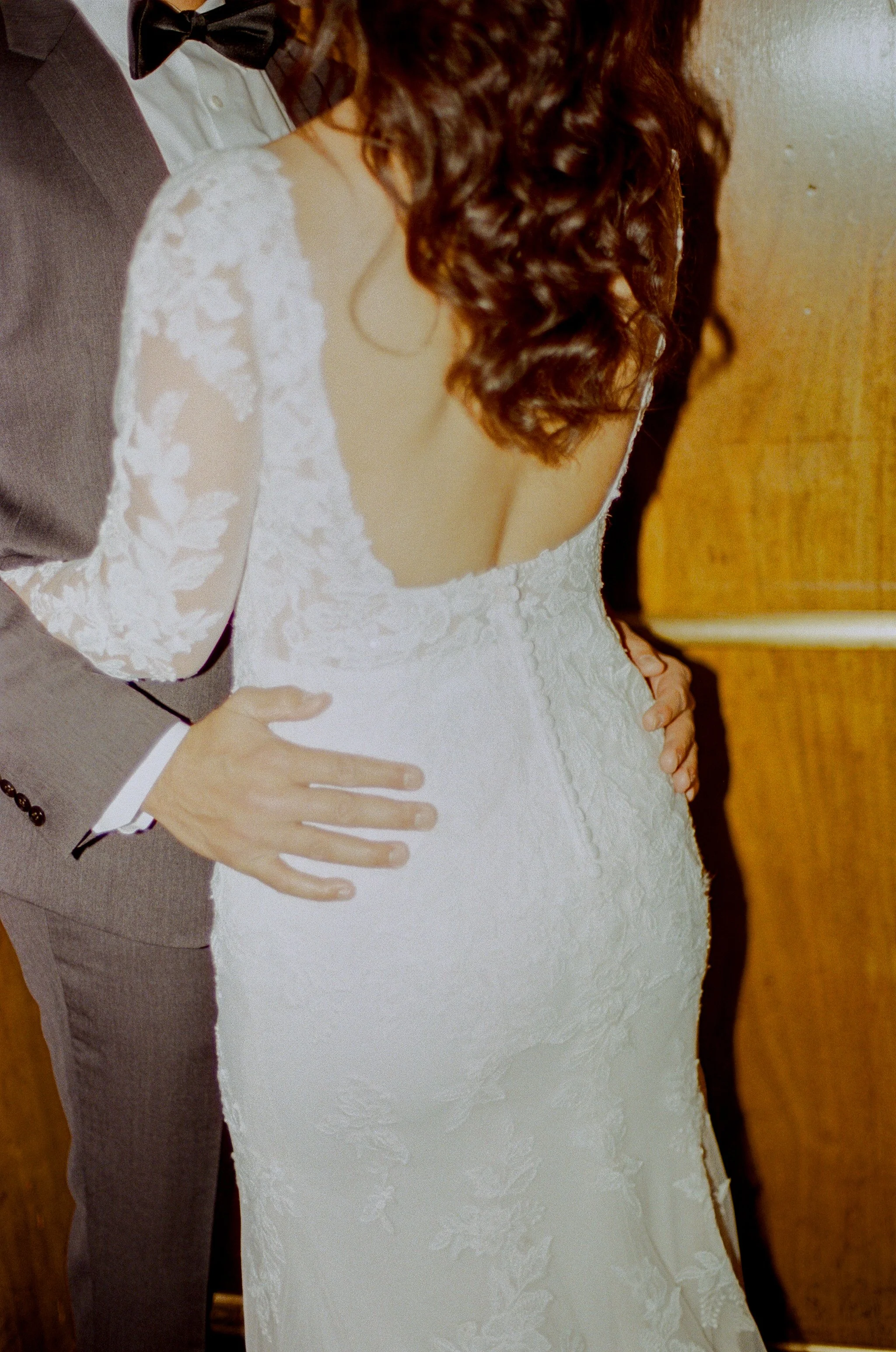 Candid close-up of the groom holding the bride around the waist, highlighting the lace details of her wedding dress.