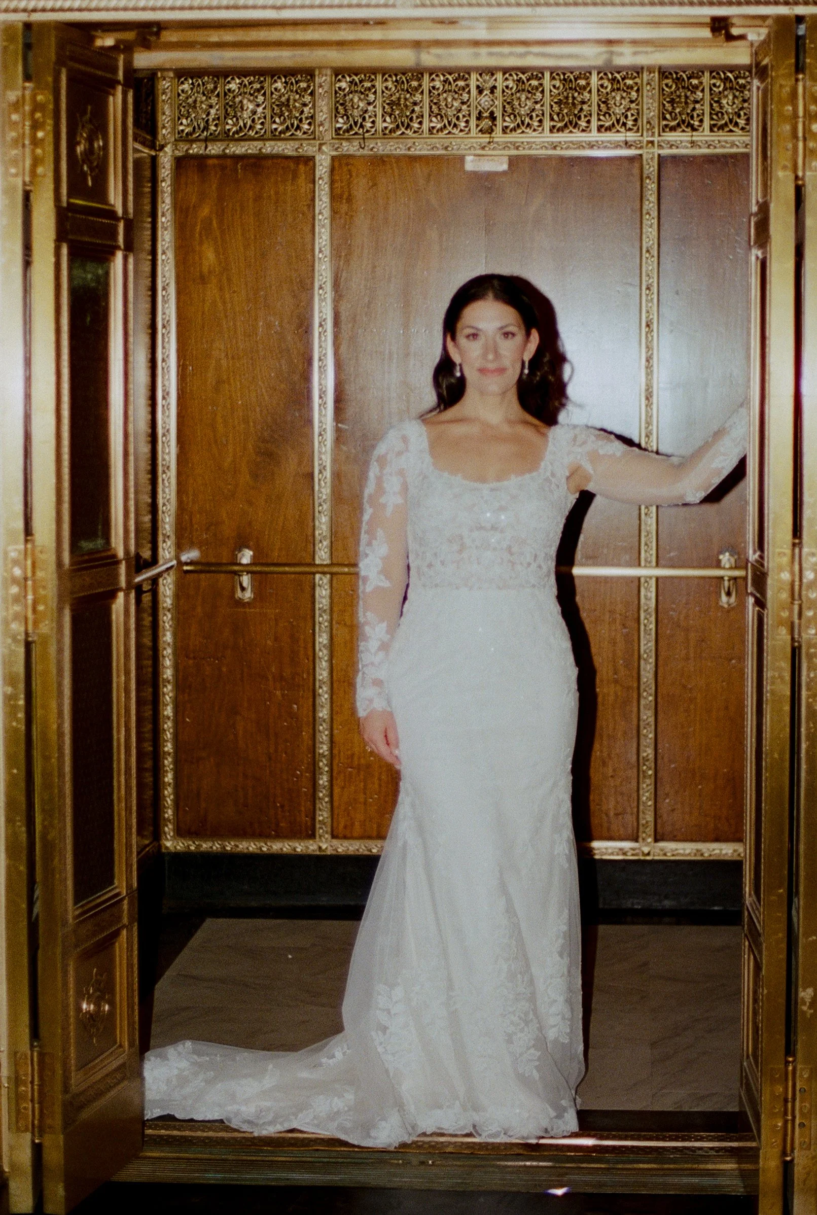 Flash portrait of the bride posing in her long-sleeve lace gown inside a vintage wood-paneled elevator during her downtown Detroit wedding.