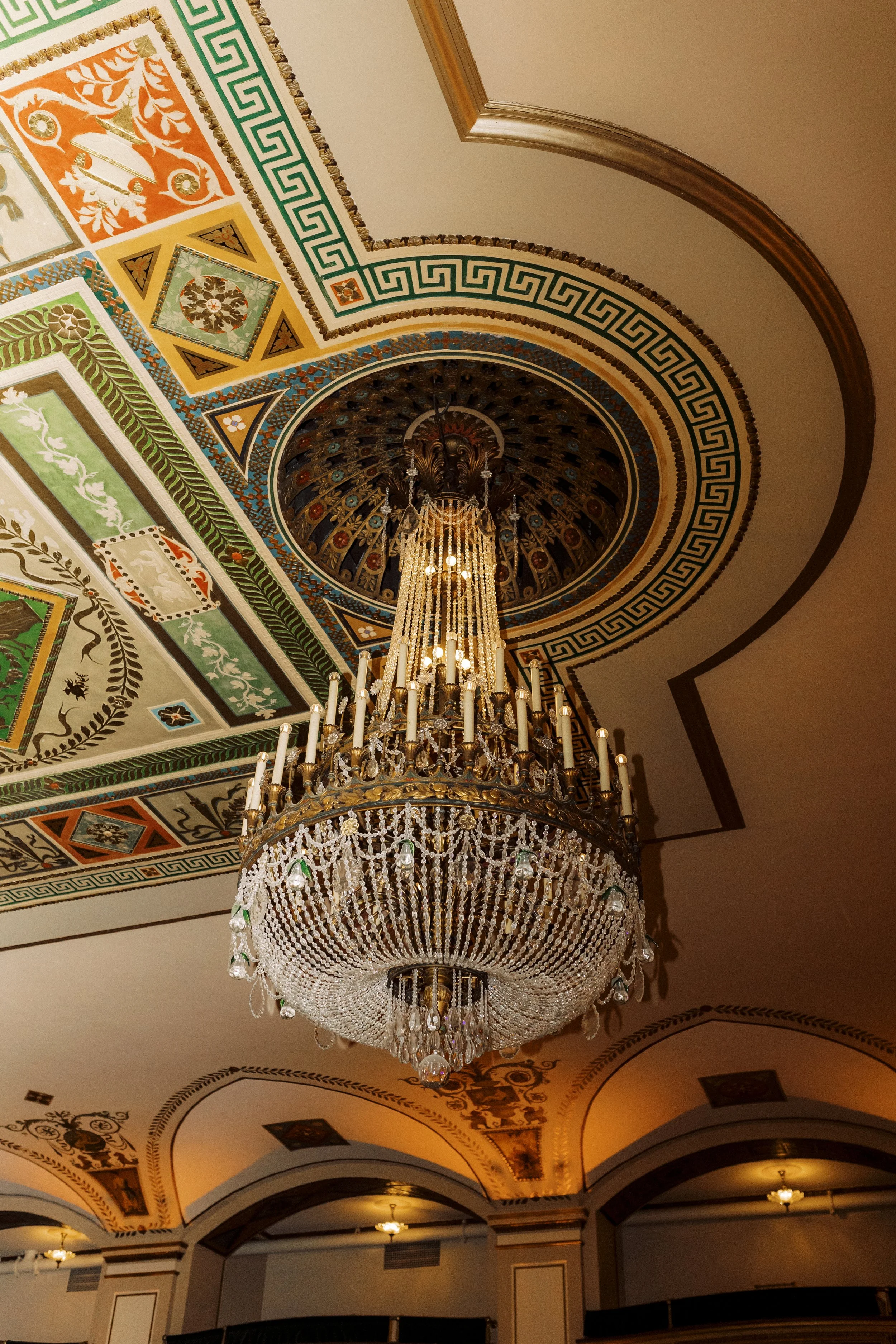 Ornate crystal chandelier and colorful painted ceiling details inside the couple’s downtown Detroit wedding venue.