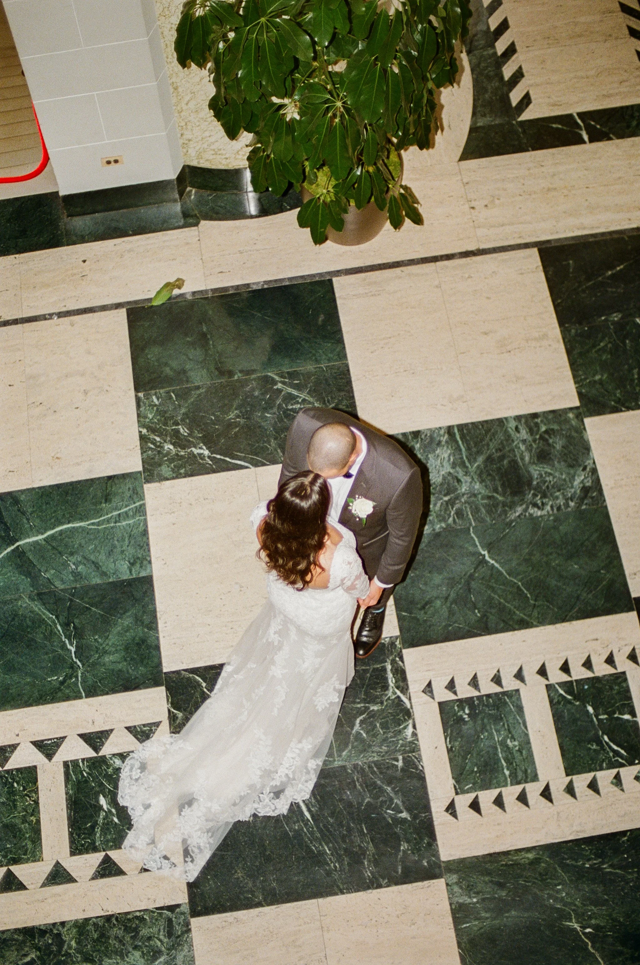 Overhead film-style photo of the bride and groom kissing on a green and white marble floor.