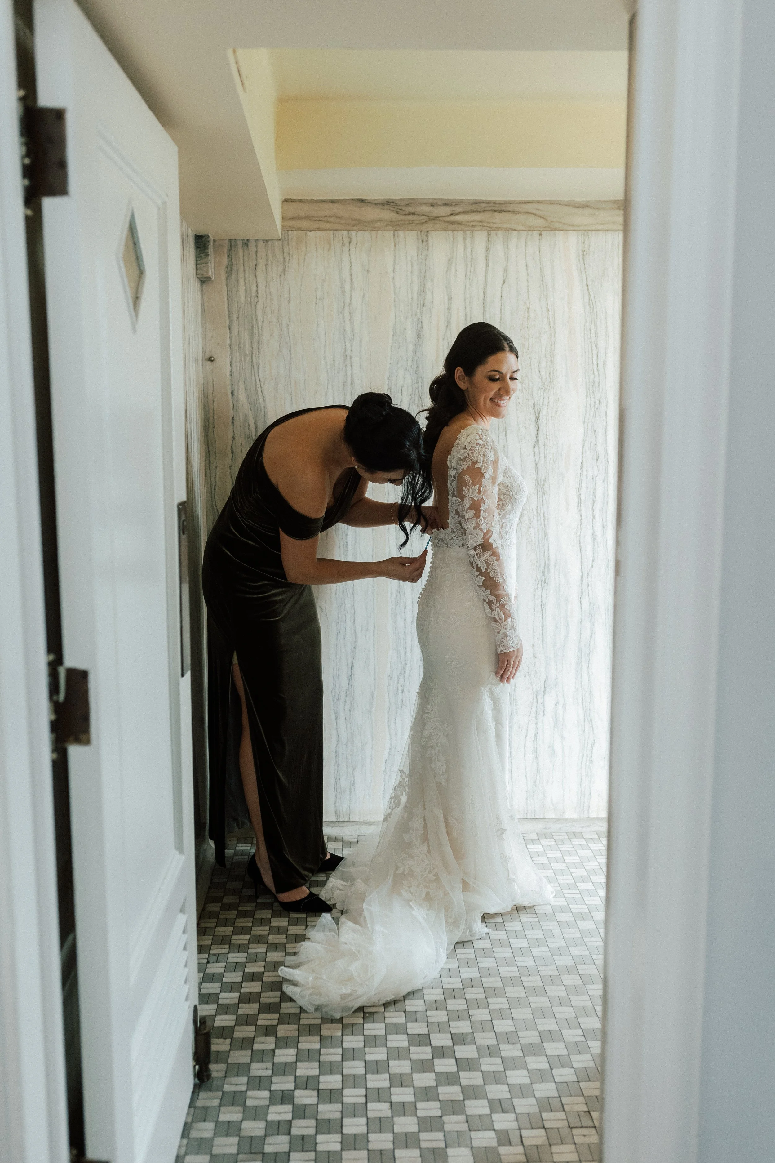 Bride having the back of her long-sleeve lace wedding dress fastened while getting ready for her downtown Detroit wedding.
