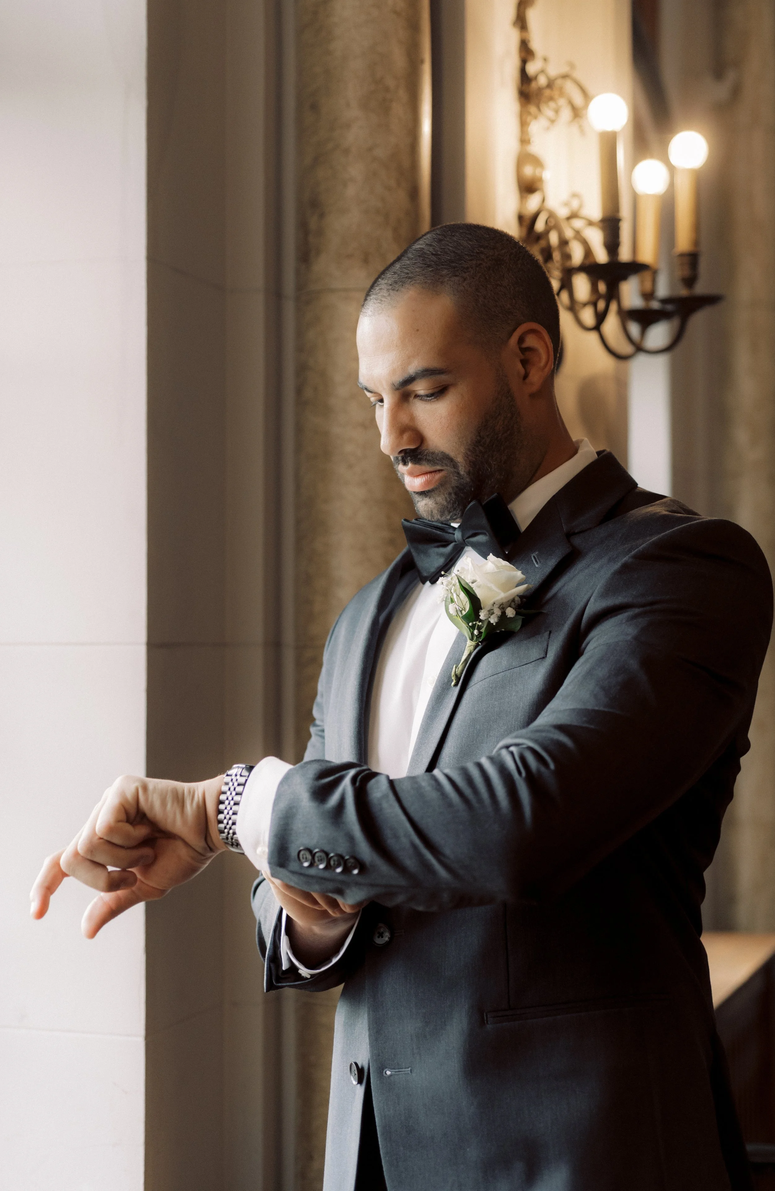 Groom adjusting his watch beside a window while getting ready for the wedding ceremony.