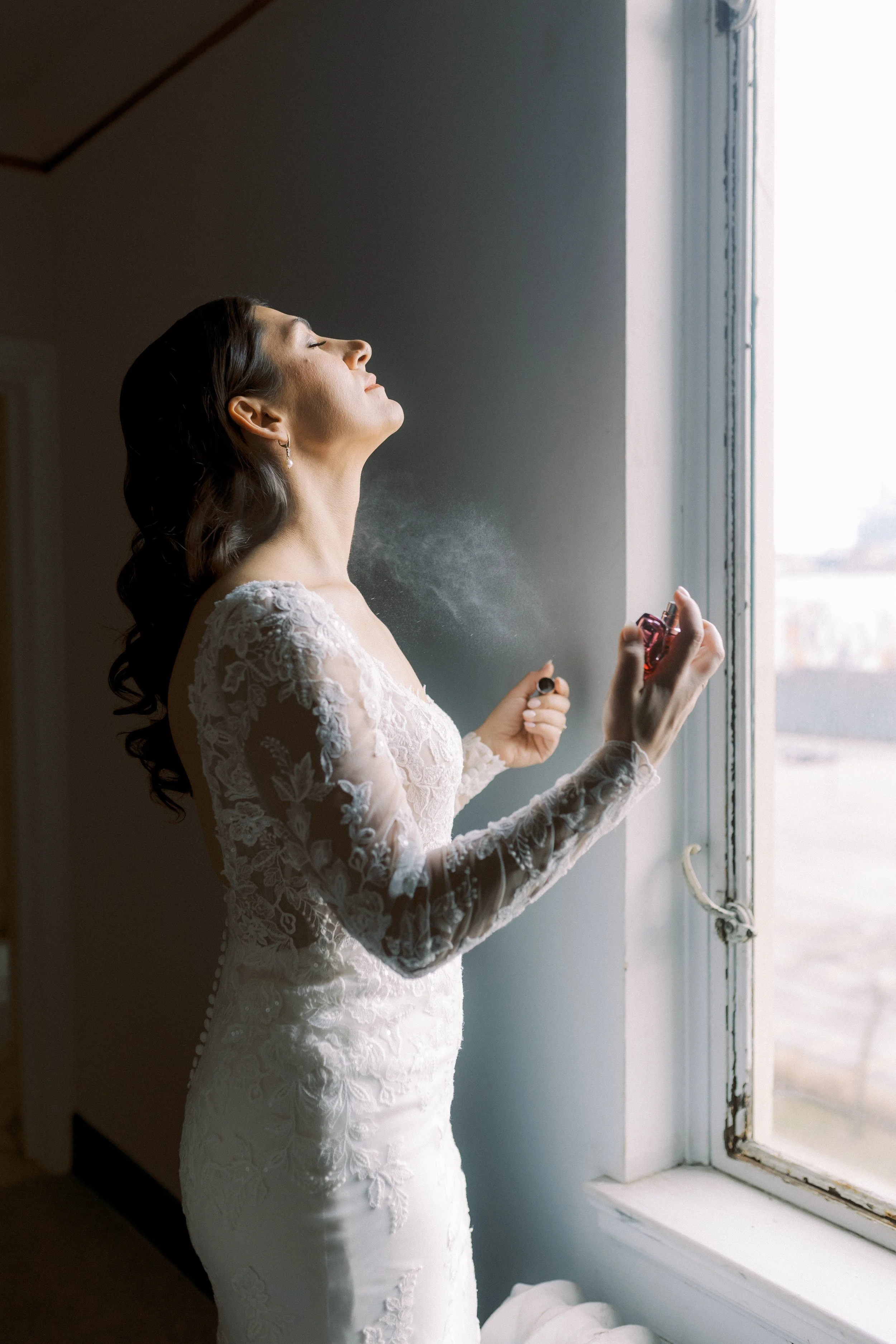 Bride spraying perfume beside a window while getting ready for her downtown Detroit wedding.