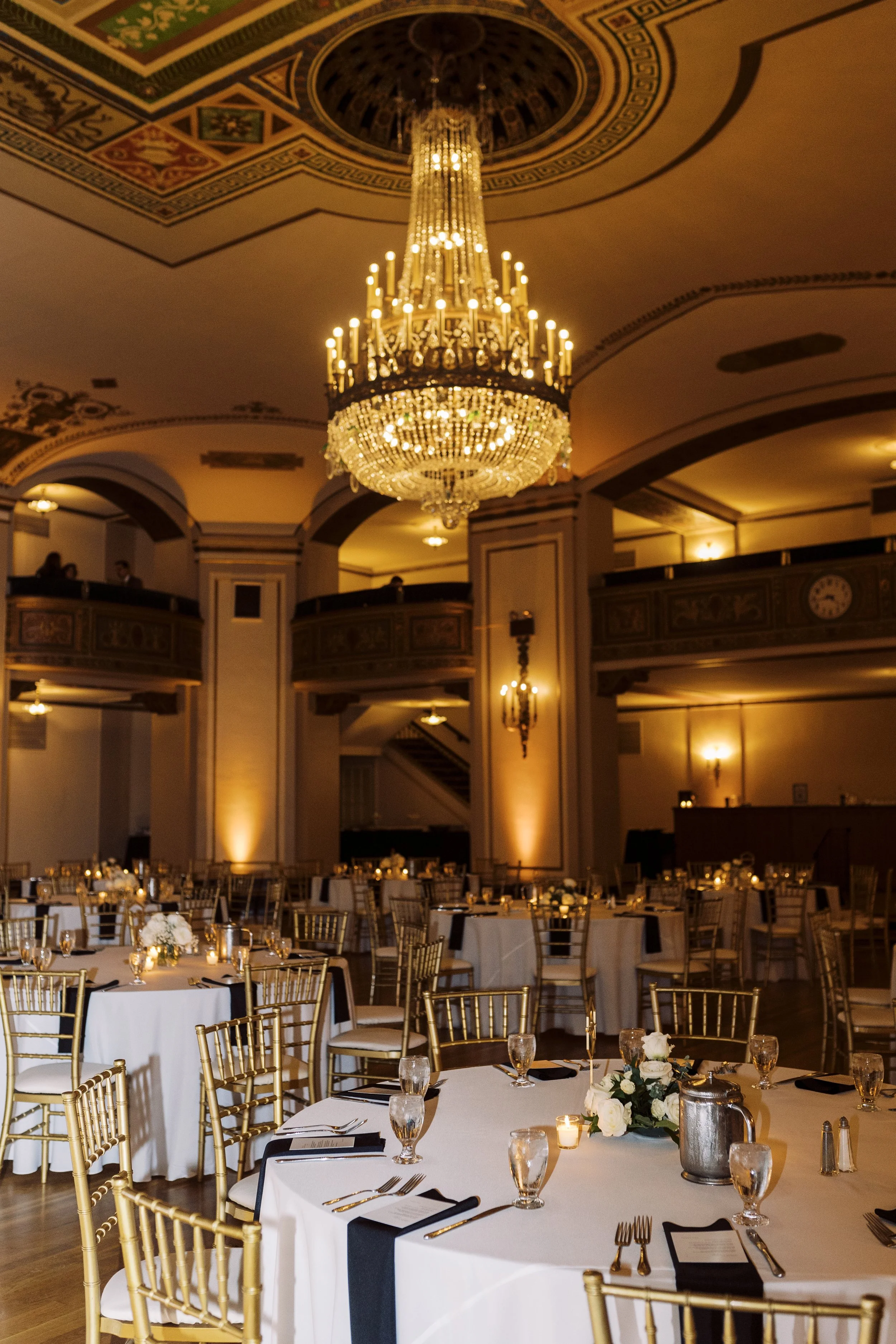 Elegant reception space with gold chairs, white linens, candlelight, and a crystal chandelier at a downtown Detroit wedding.