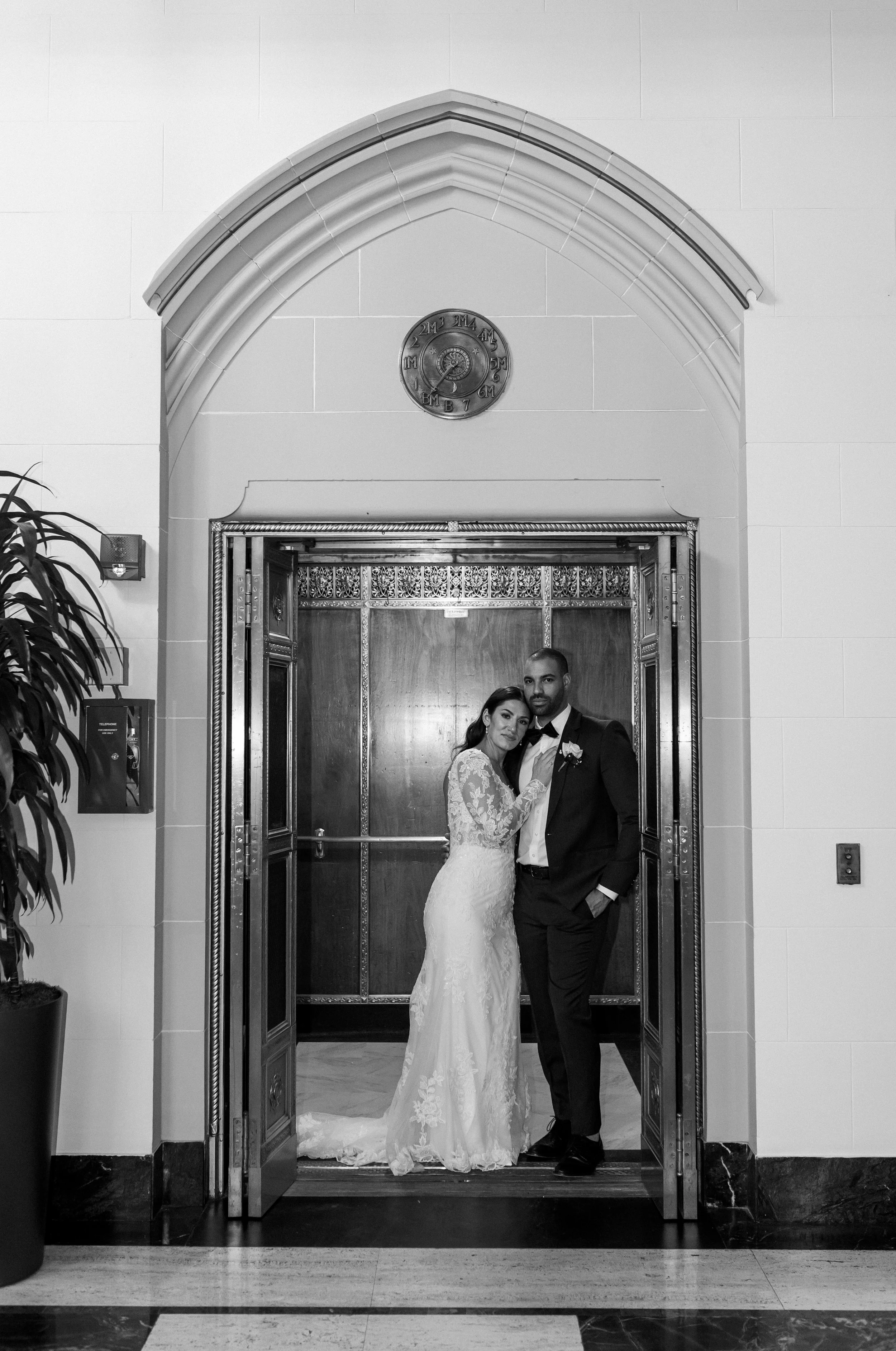 Black and white image of a bride and groom standing in an ornate elevator