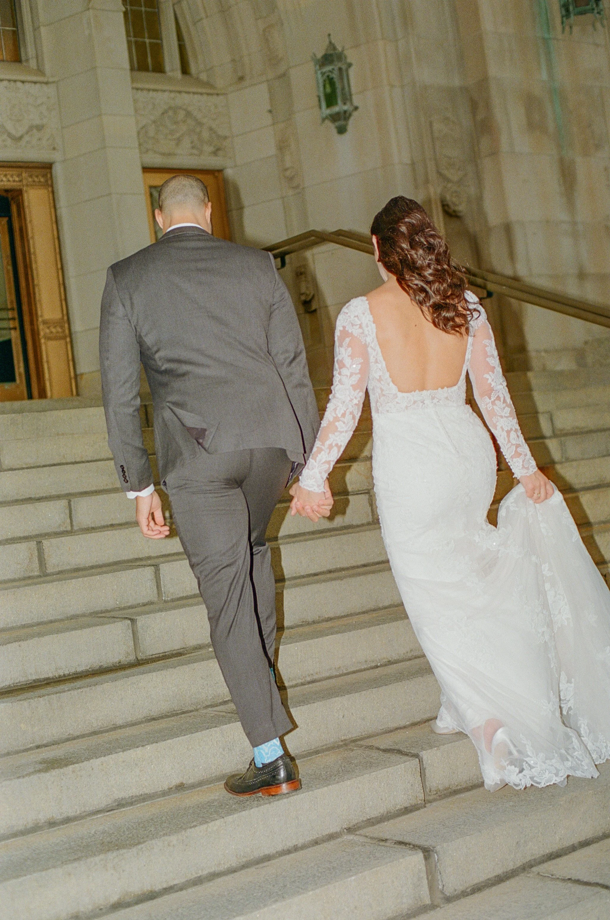 A bride and groom go up the steps of their venue at their downtown Detroit wedding while holding hands