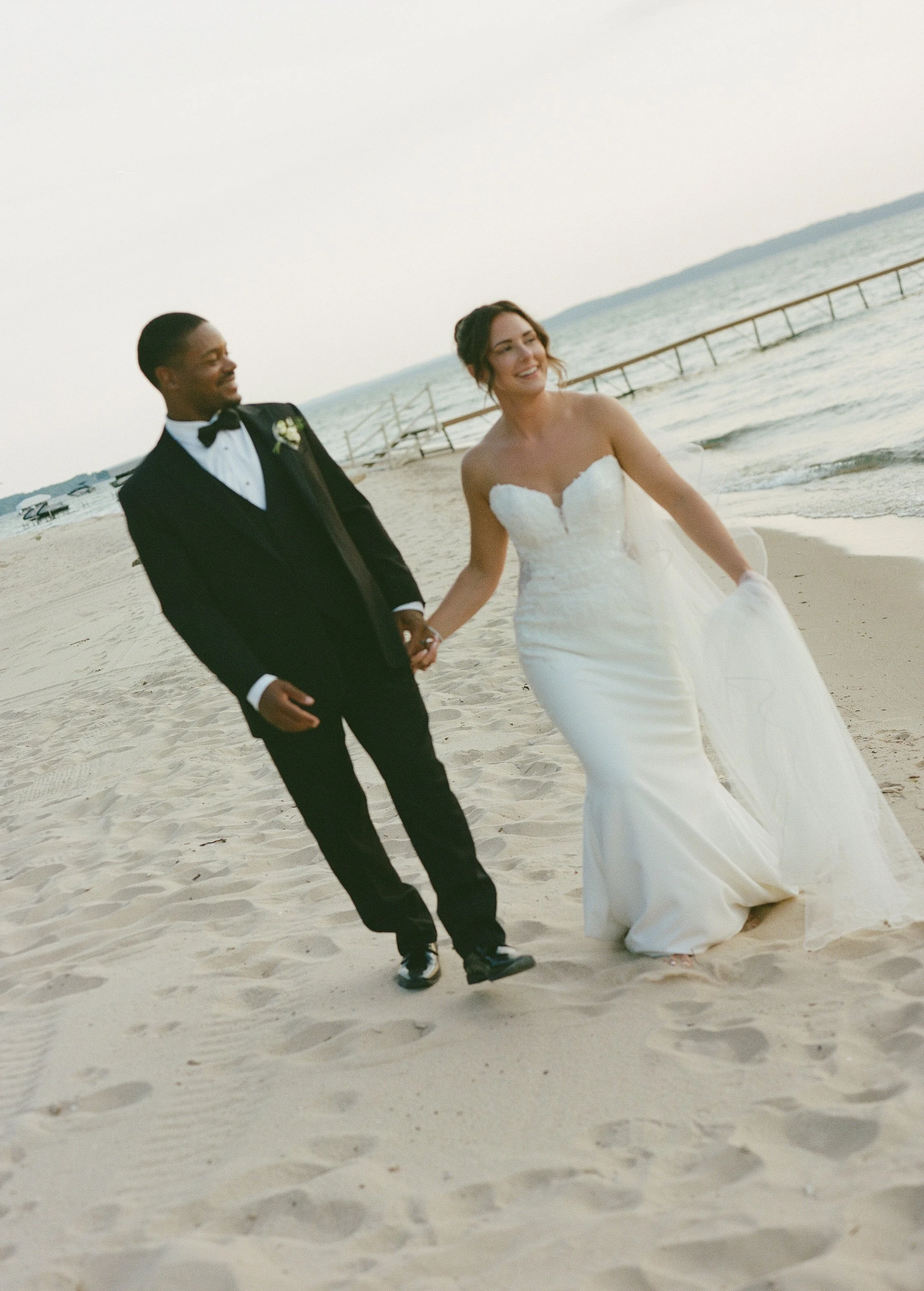 Bride and groom walking hand in hand along the sandy lakeshore after their wedding ceremony.