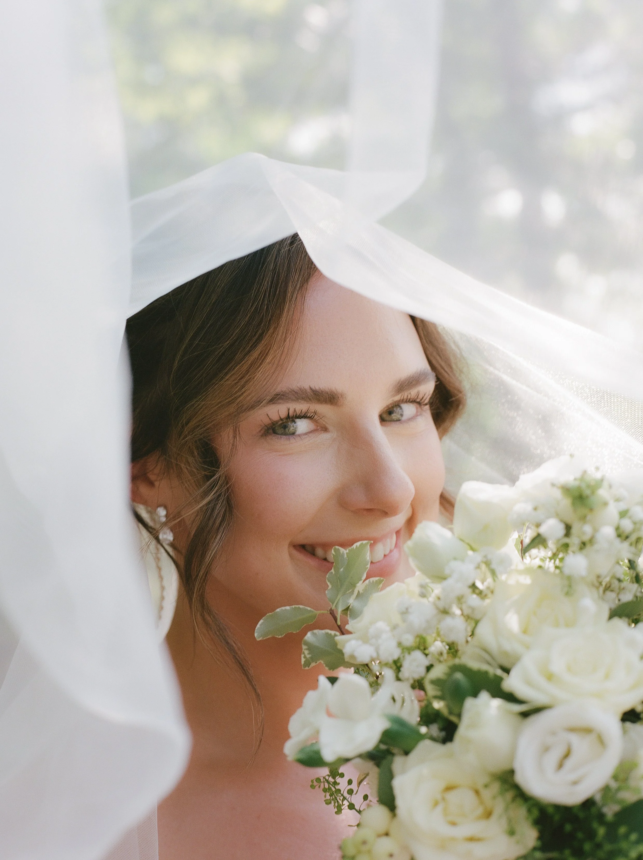 Close-up bridal portrait beneath her veil holding a white floral bouquet at a Northern Michigan backyard wedding.