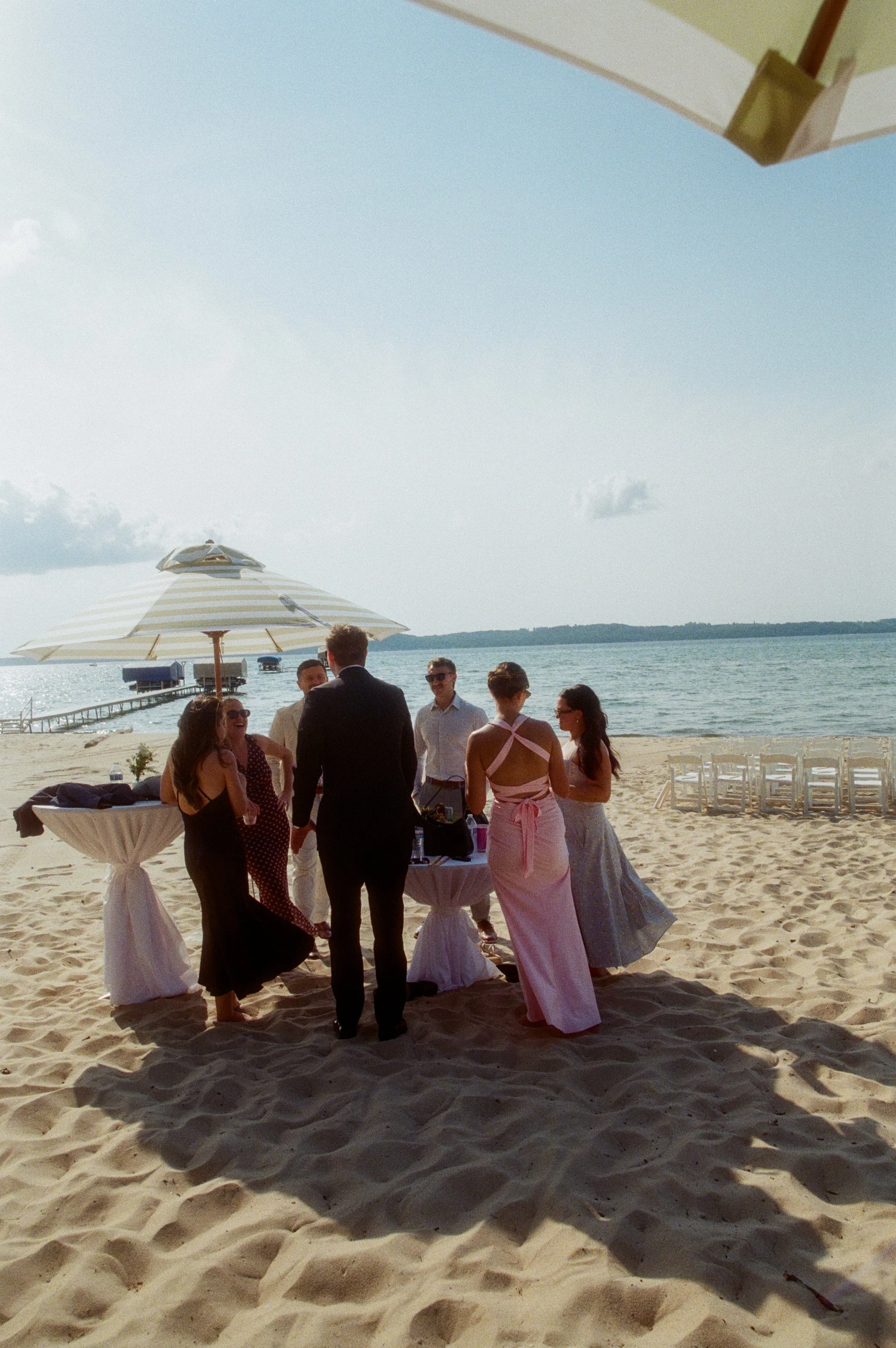 Wedding guests mingling at a cocktail table on the beach during a Northern Michigan backyard wedding.
