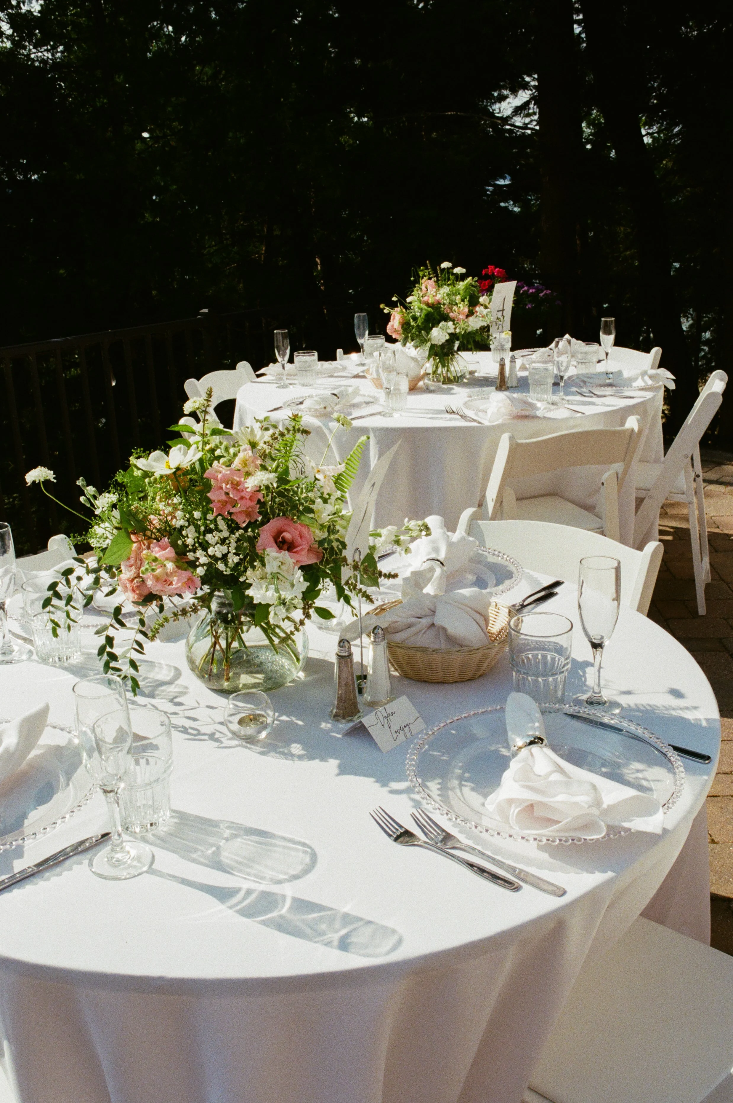 Outdoor reception tables decorated with colorful garden-inspired florals and white linens at a Northern Michigan backyard wedding.