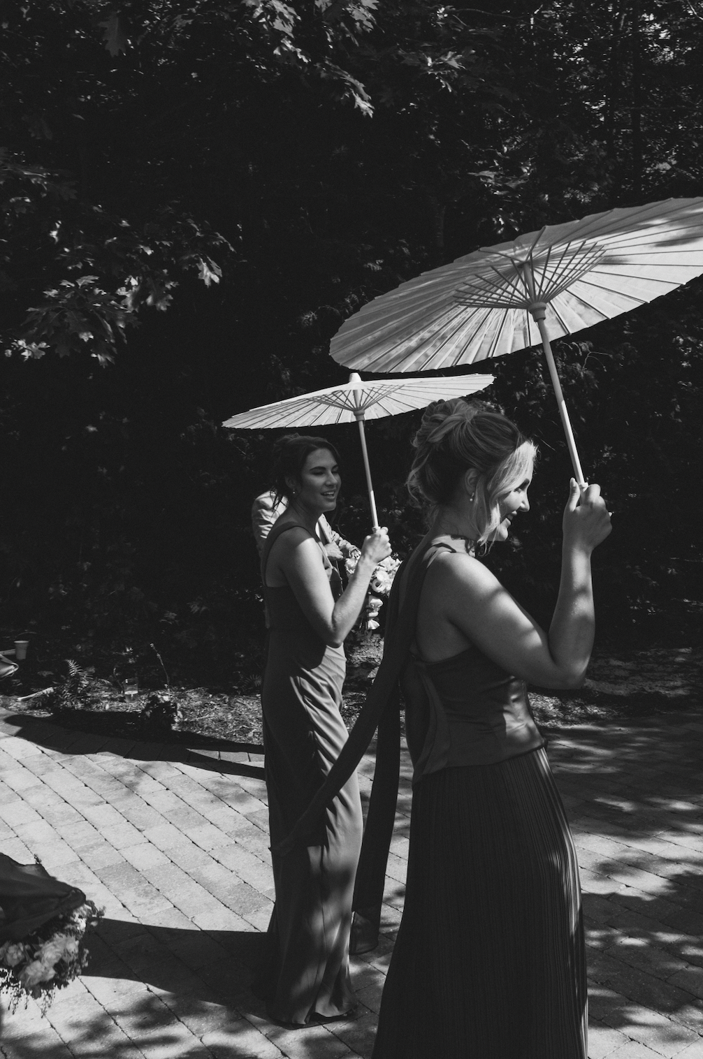 Black and white candid photo of bridesmaids carrying parasols outside before the ceremony.
