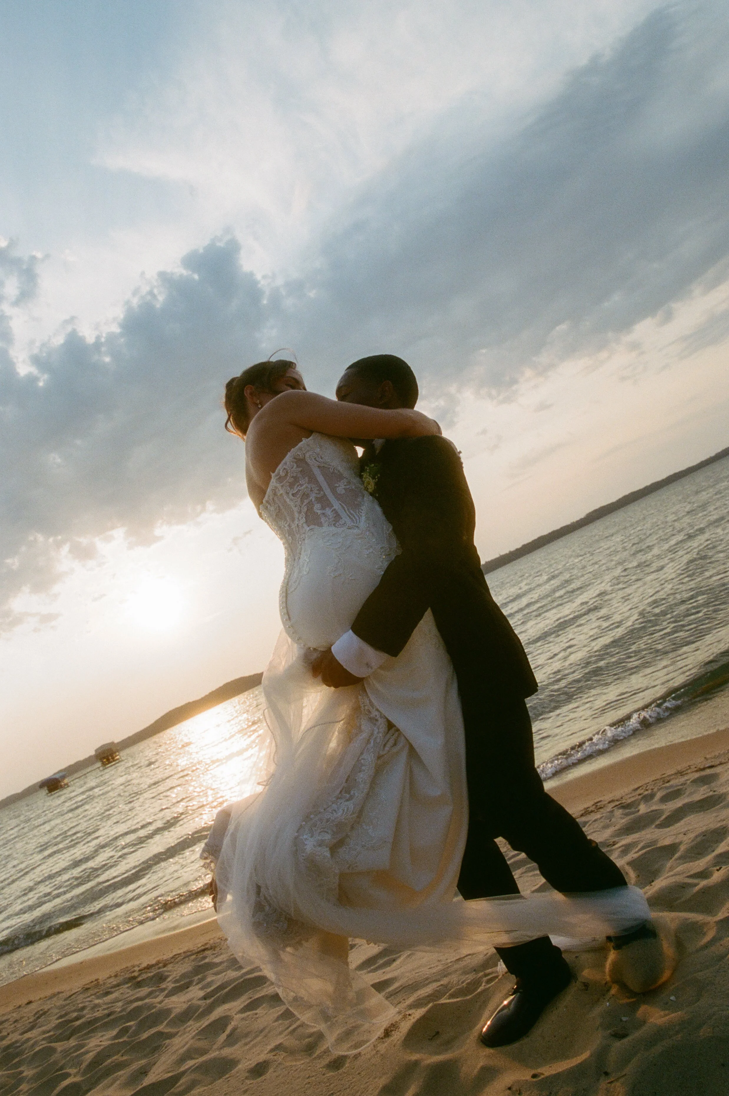 Newlyweds embracing on the beach at sunset during their Northern Michigan backyard wedding.