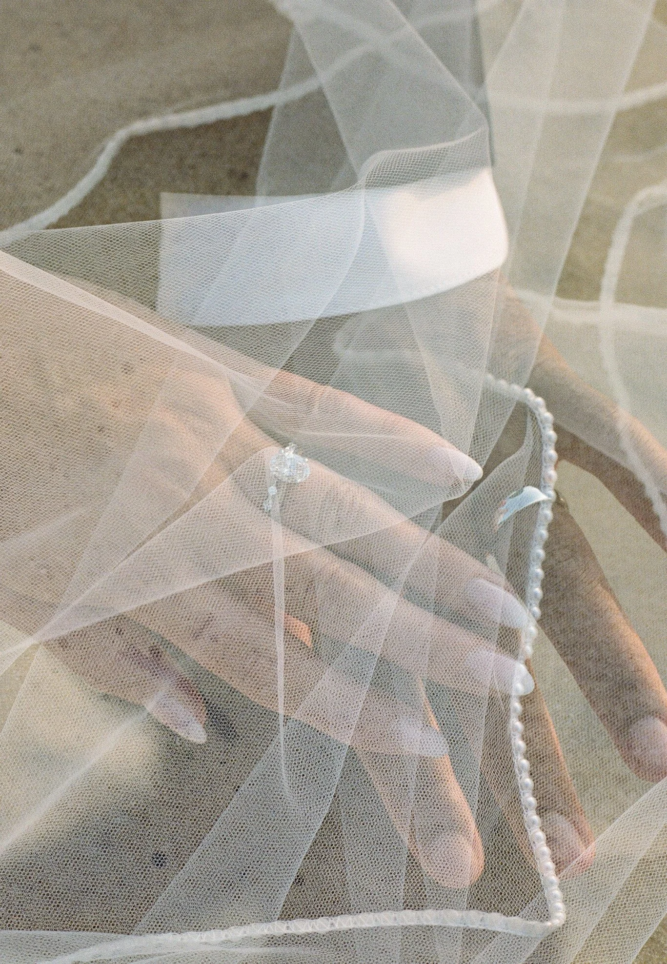 Close-up of the bride’s engagement ring and pearl bracelet beneath her veil at a Northern Michigan backyard wedding.