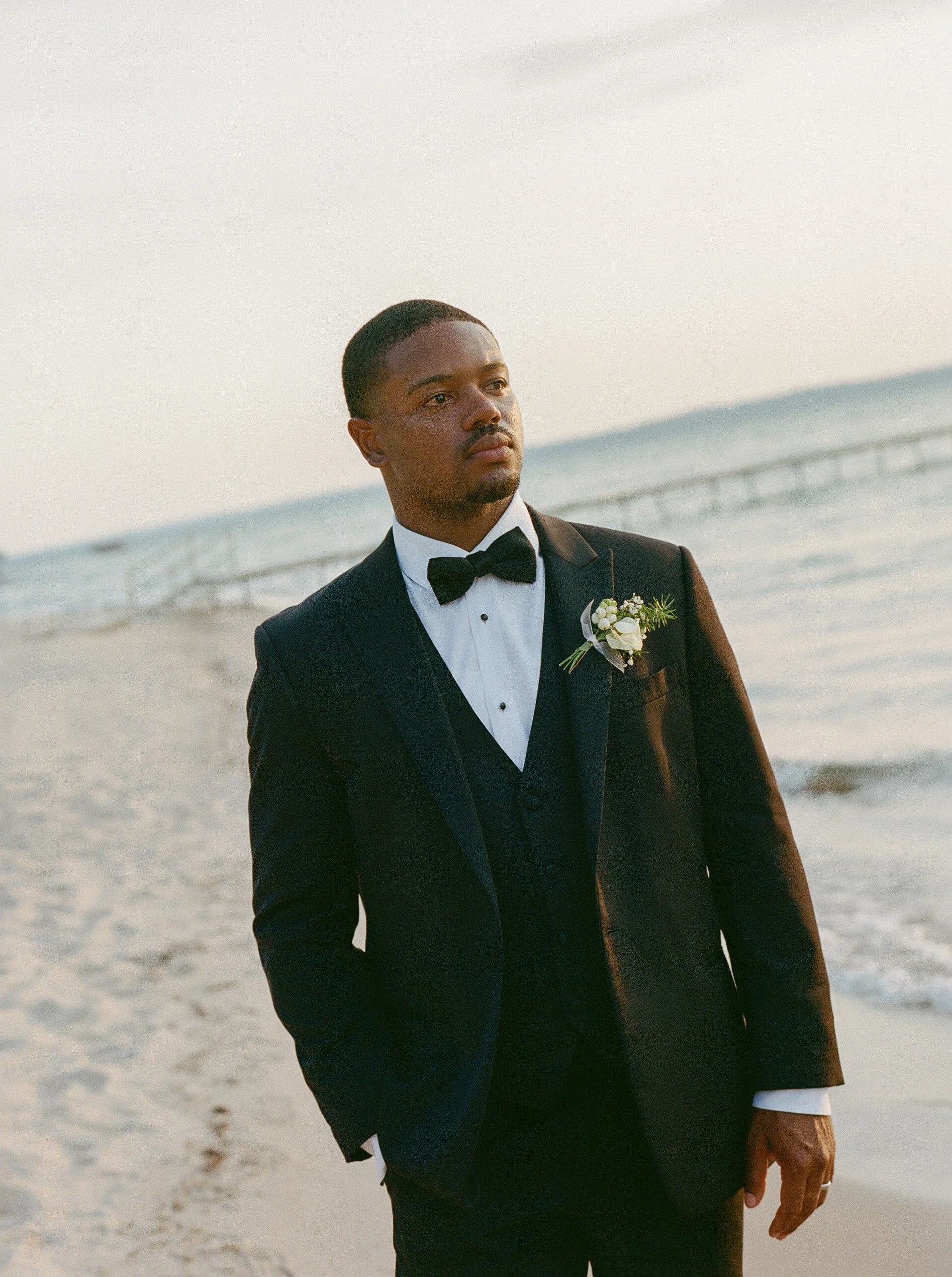 Groom portrait in a black tuxedo along the lakeshore during a Northern Michigan backyard wedding.
