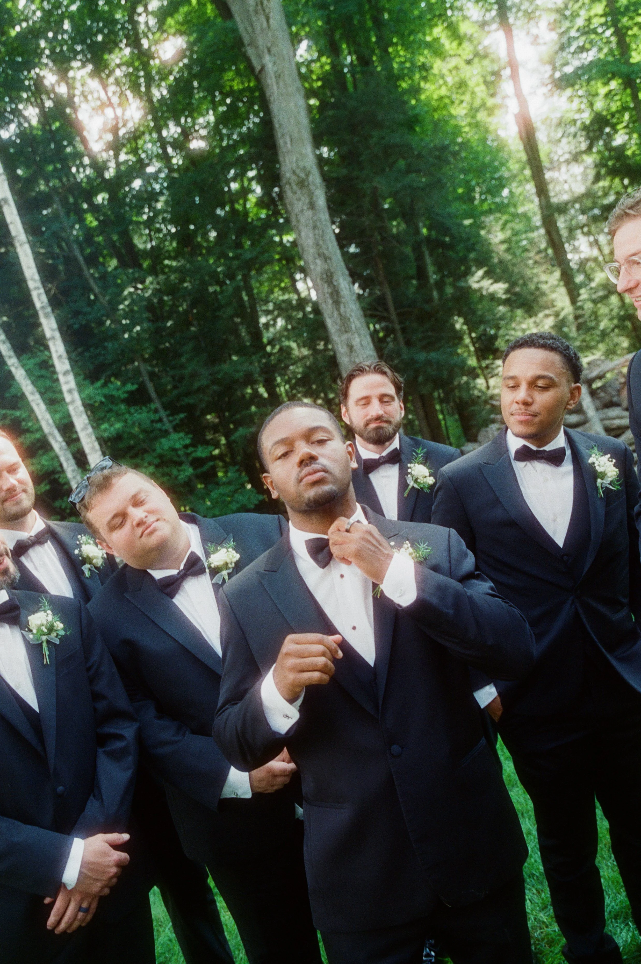 Groom adjusting his bow tie while surrounded by his groomsmen outdoors.