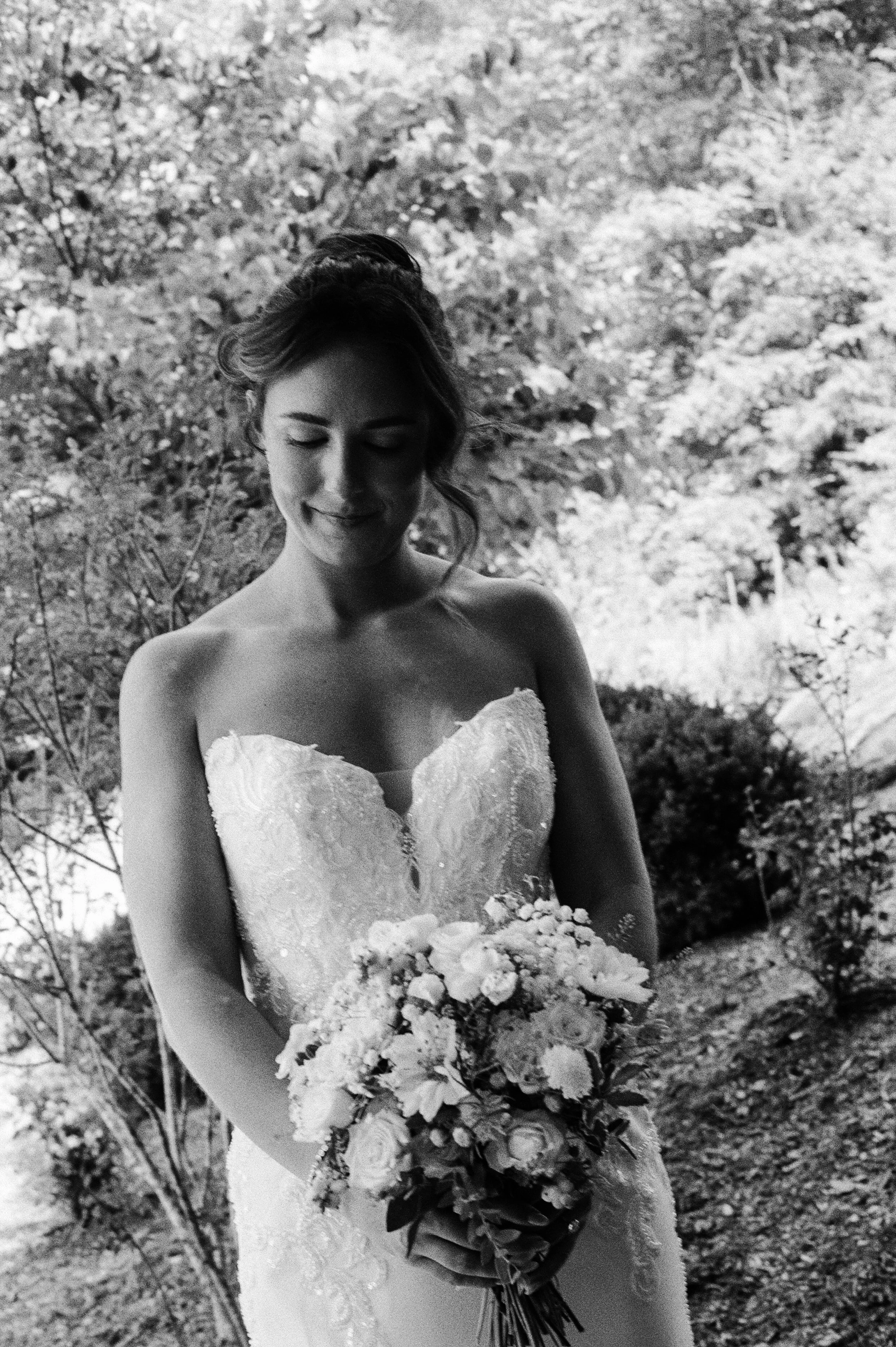 Black and white bridal portrait of the bride holding her bouquet outdoors.