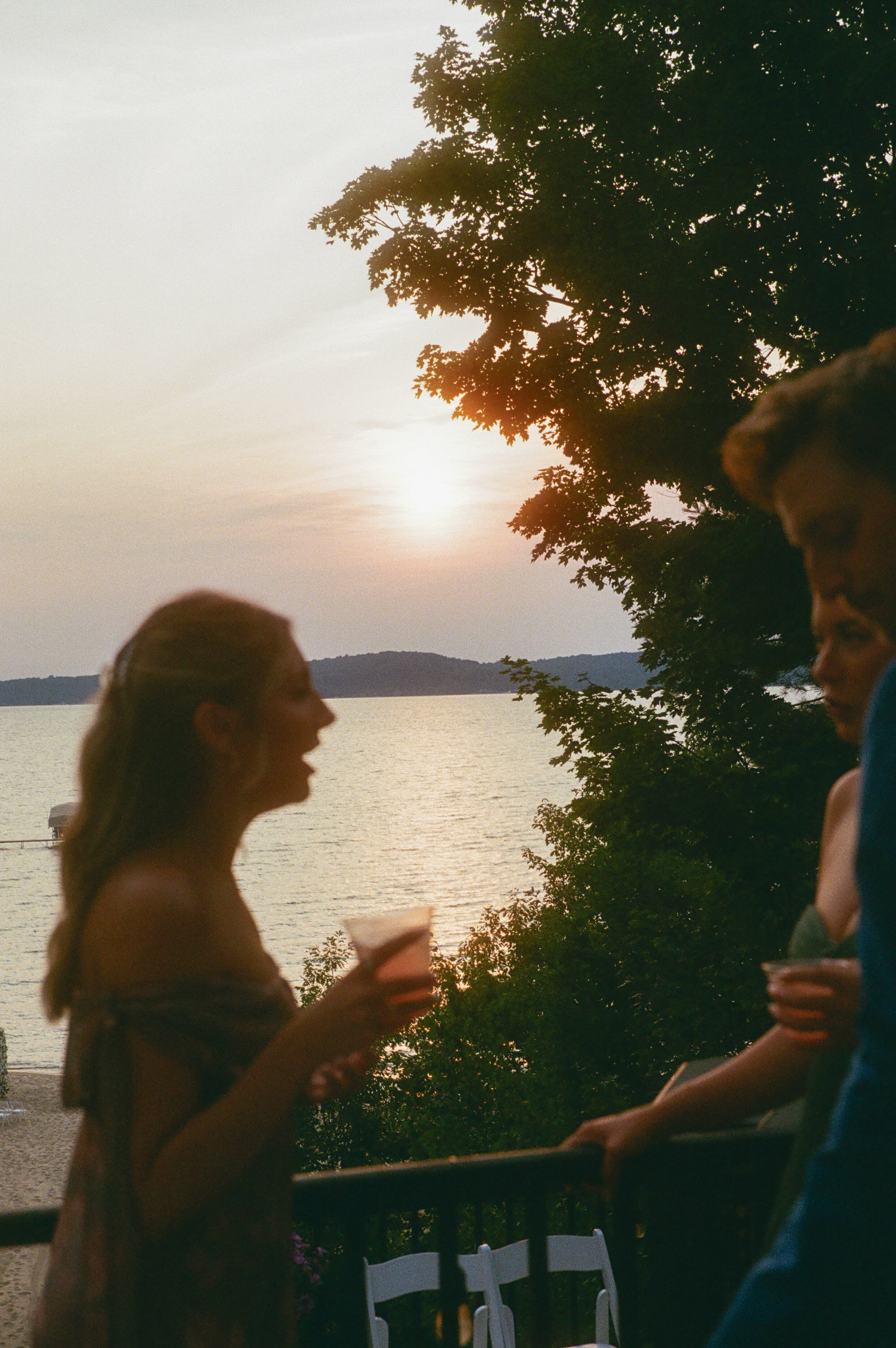 Wedding guest enjoying a drink at sunset with the lake glowing in the background.