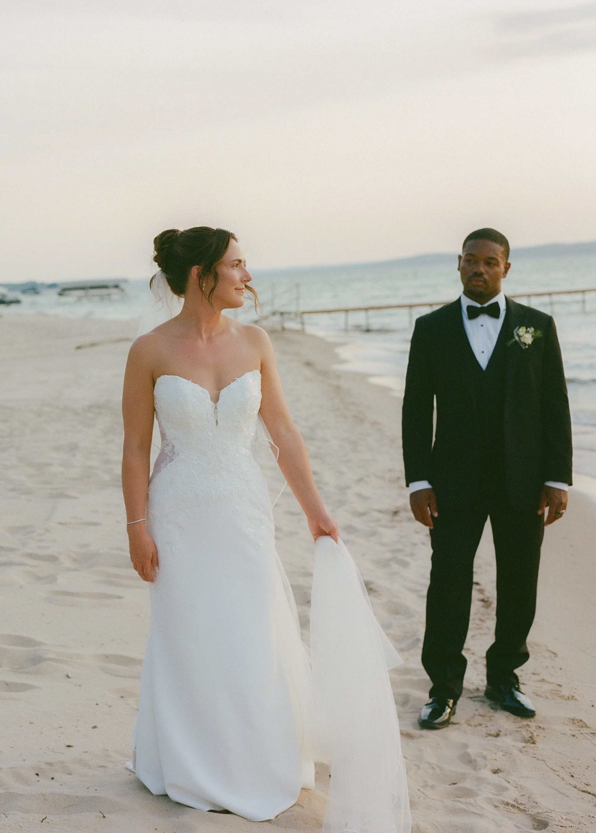 Bride and groom posing on the sandy lakeshore in their wedding attire.