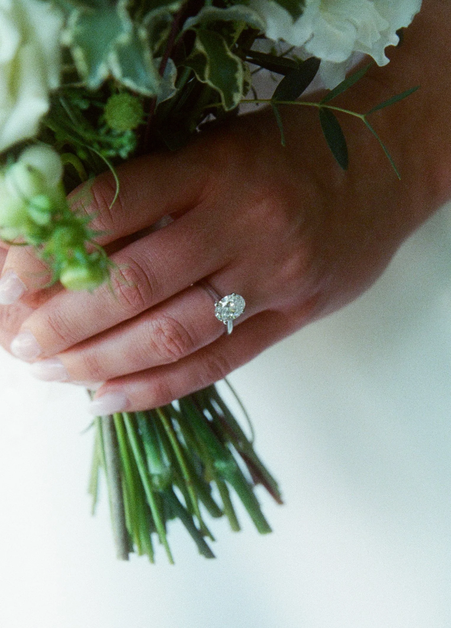 A close up of a brides engagement ring as she is holding her wedding bouquet.
