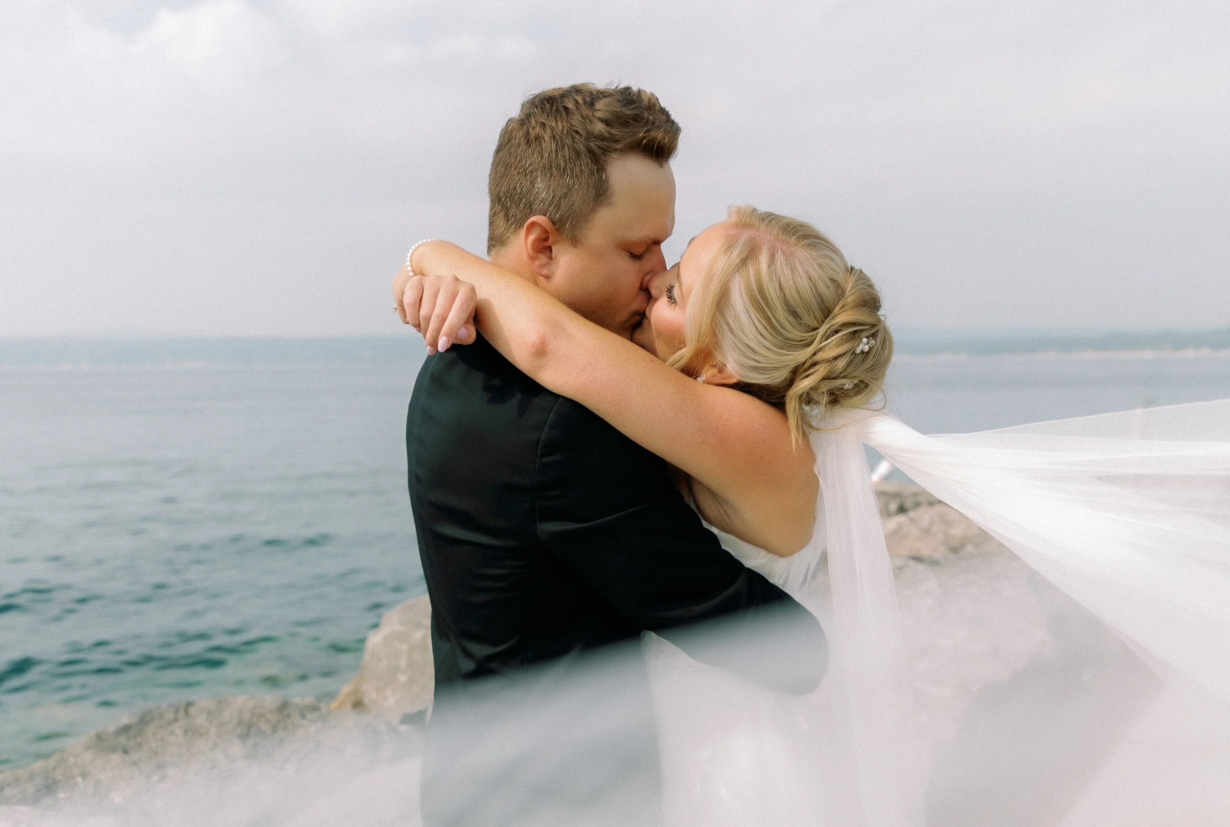 Close-up of the bride and groom sharing a kiss by the water during their wedding portraits.