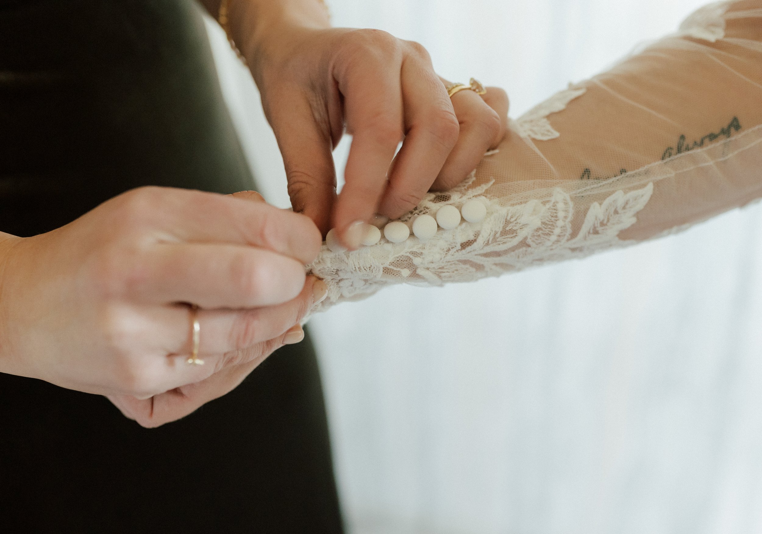 Close-up of the delicate buttons being fastened along the bride’s lace wedding dress sleeve.