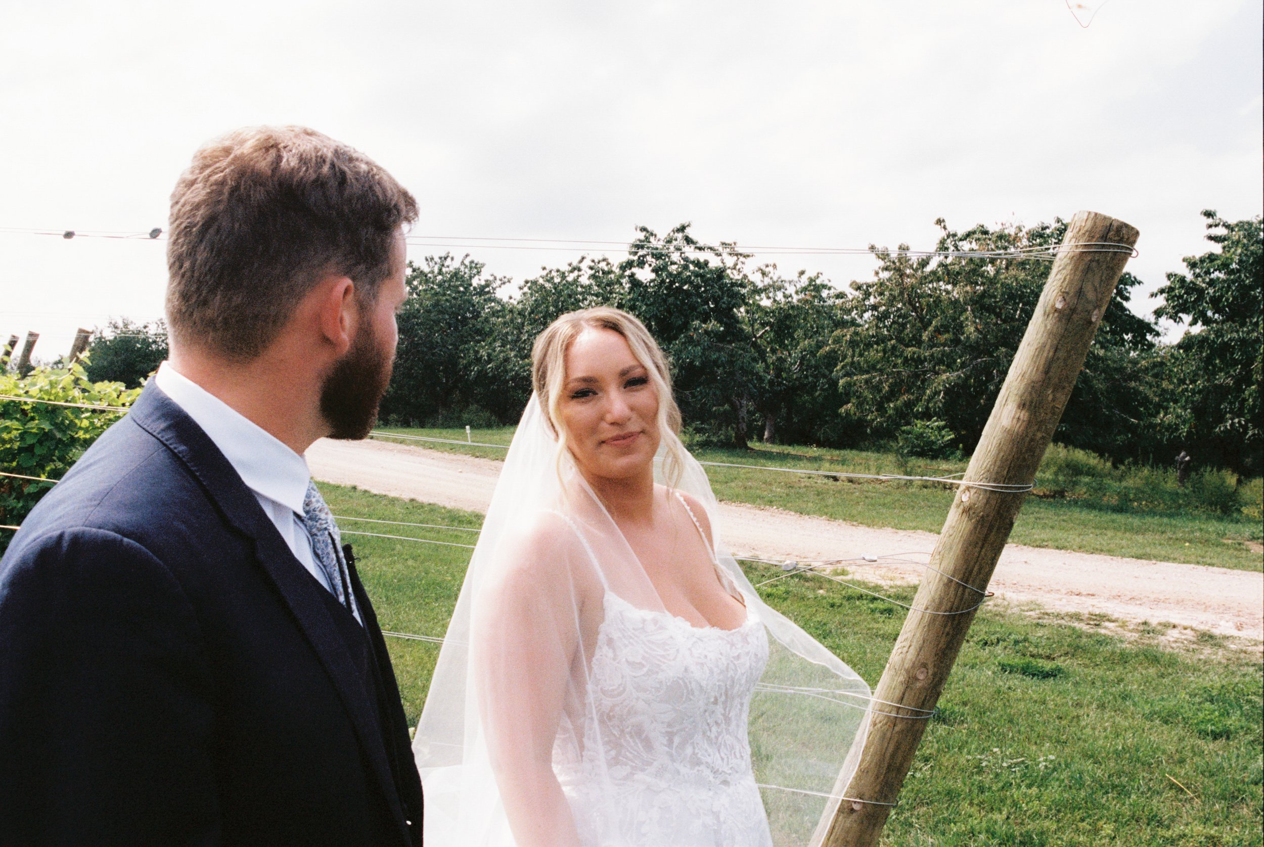 Bride smiling at her groom during portraits at a Northern Michigan vineyard wedding surrounded by lush greenery and vines.