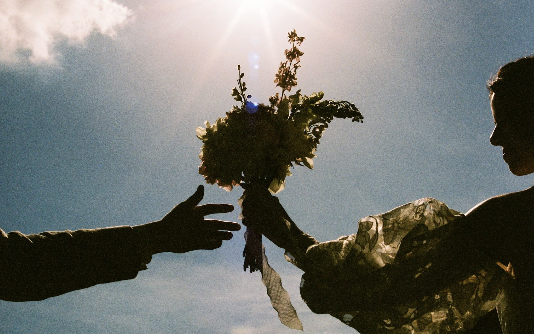 A silhouette of a bride and grooms hands as the bride is passing her bouquet to her groom.