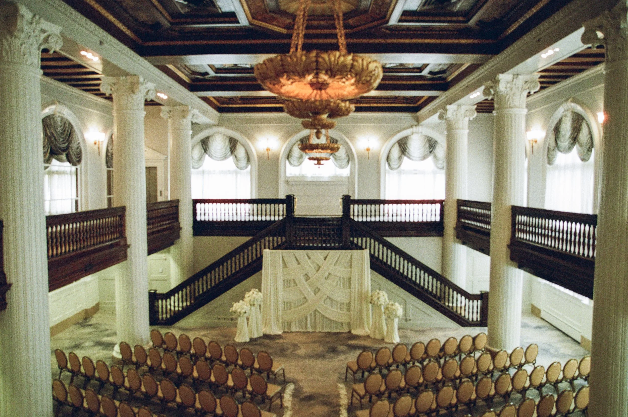 Wide view of an elegant wedding ceremony setup inside a historic ballroom captured with cinematic film photography aesthetics