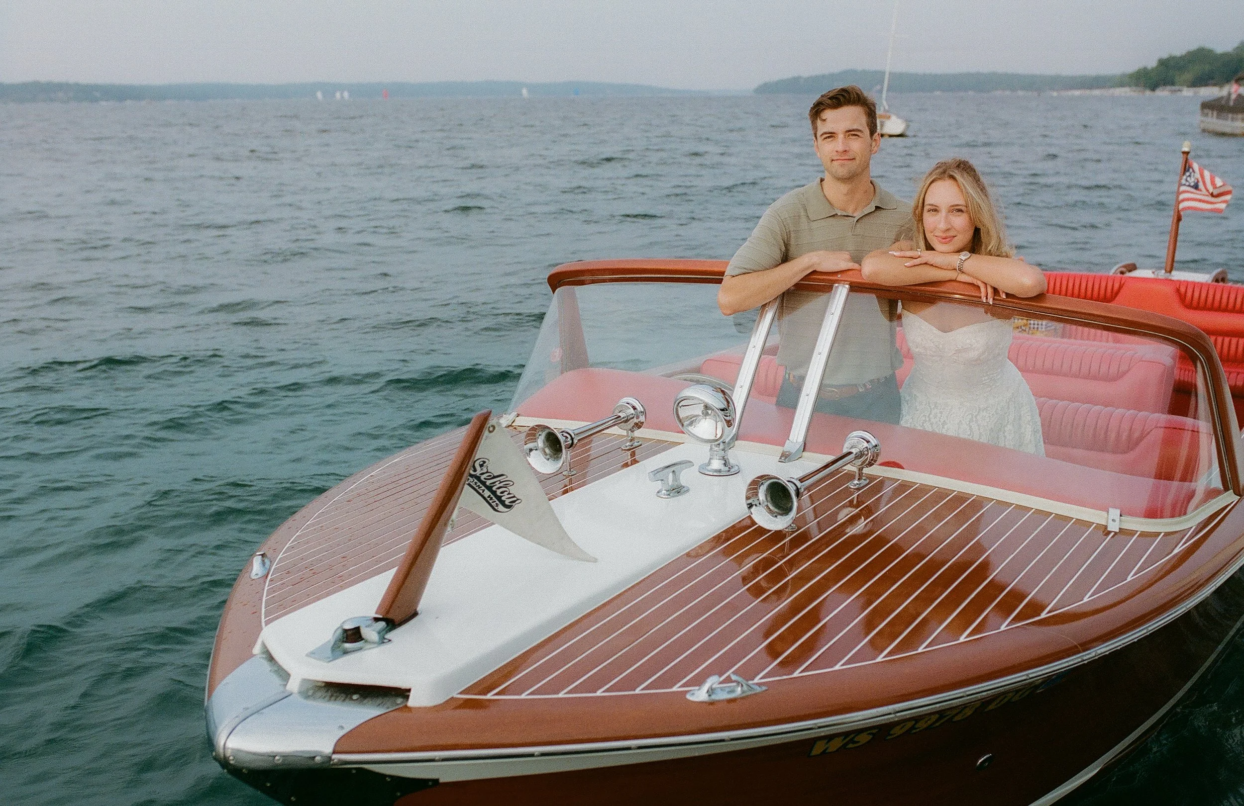 Couple leaning against the windshield of a classic wooden boat during their Lake Geneva Engagement session on the water.