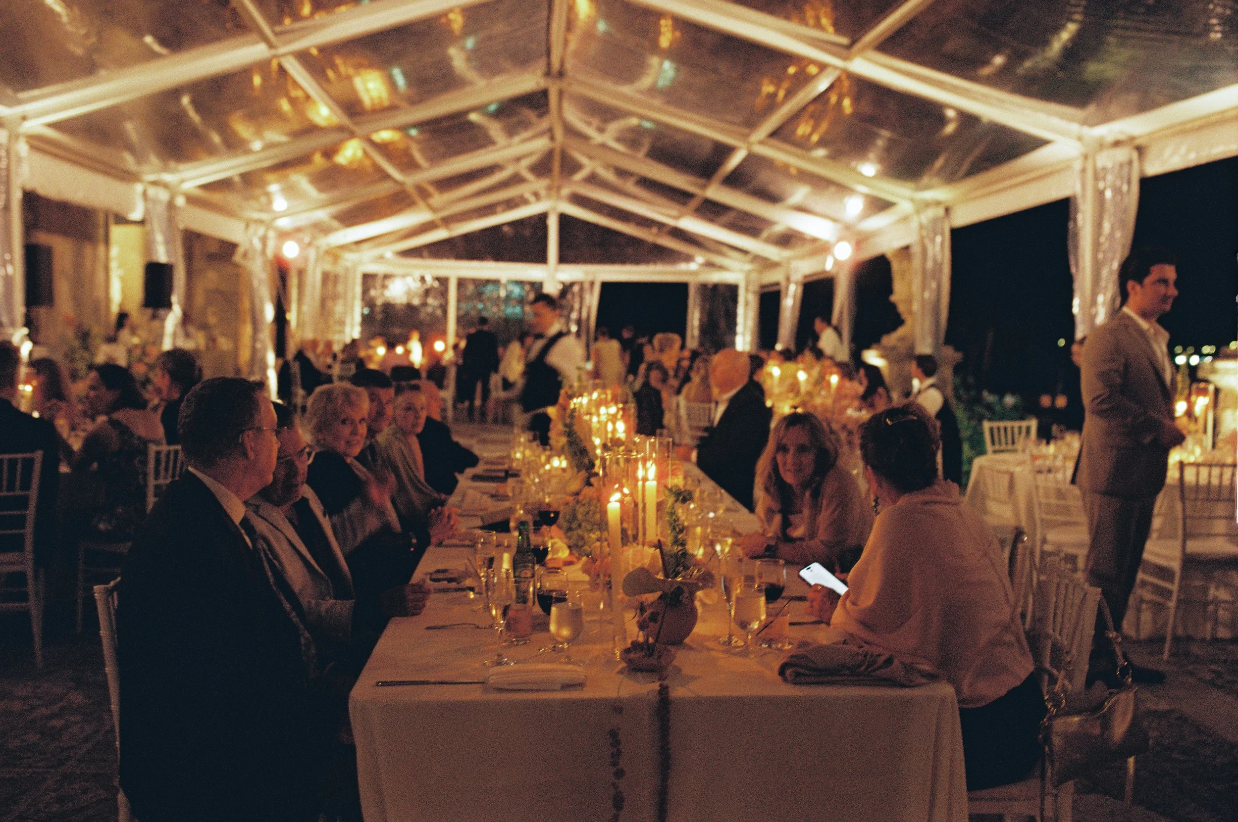 Candlelit reception dinner inside a clear tent with long tables, glowing candles, and guests gathered together during a Vizcaya Museum and Gardens wedding.