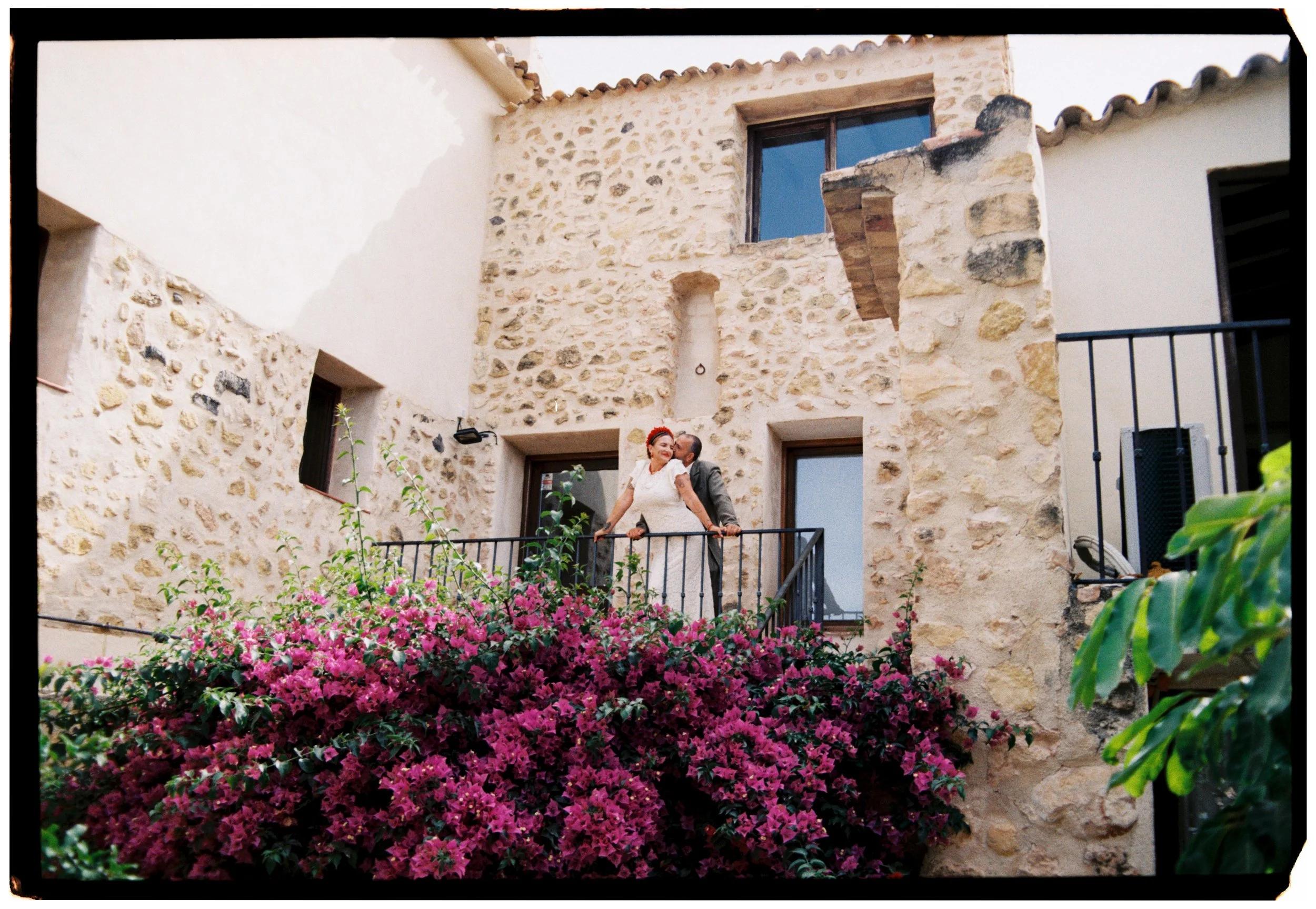 Newlyweds sharing a quiet moment on a balcony above blooming bougainvillea during their Spain wedding.