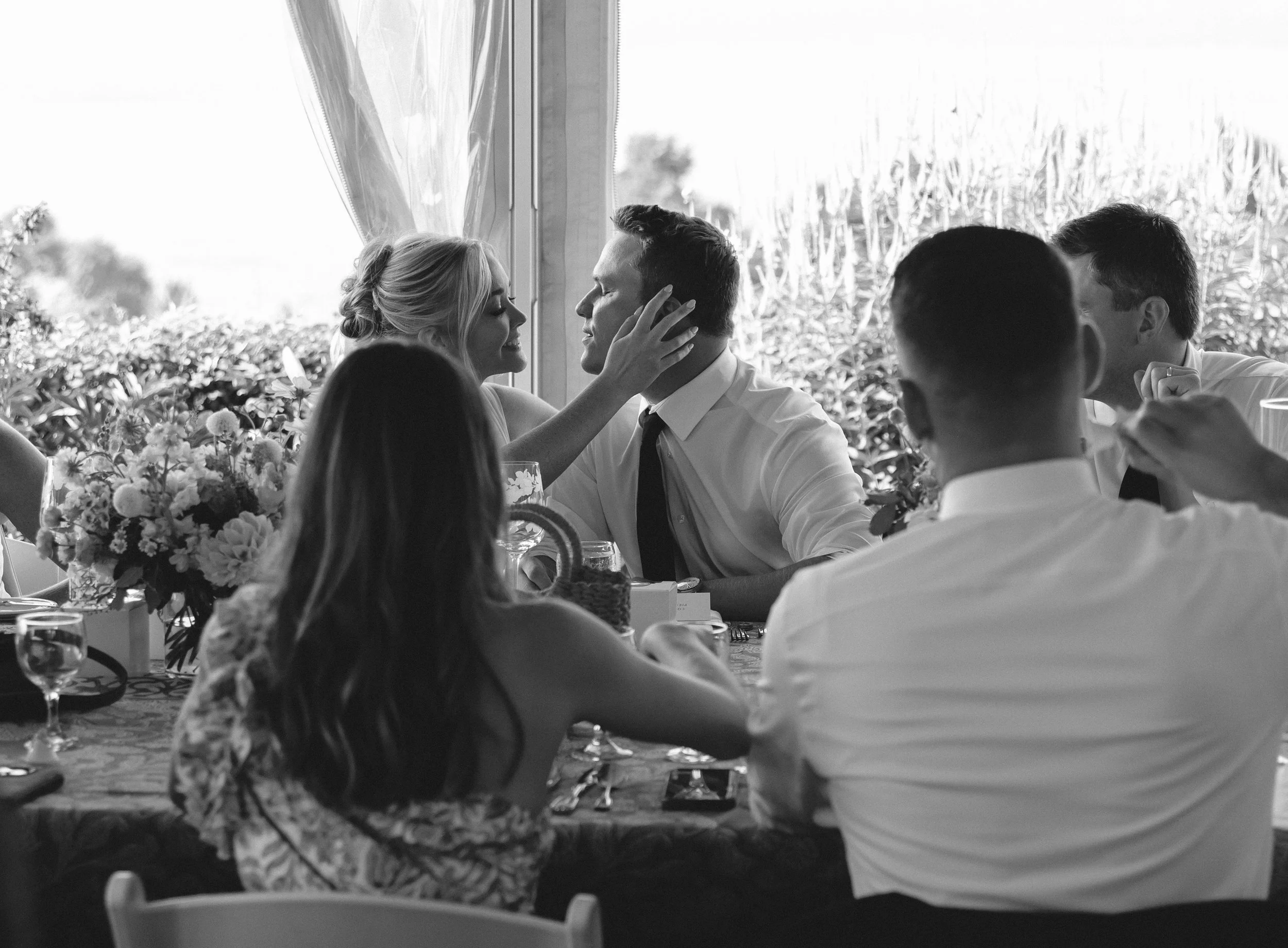 Bride gently touching the groom's face during an intimate reception moment by the window.