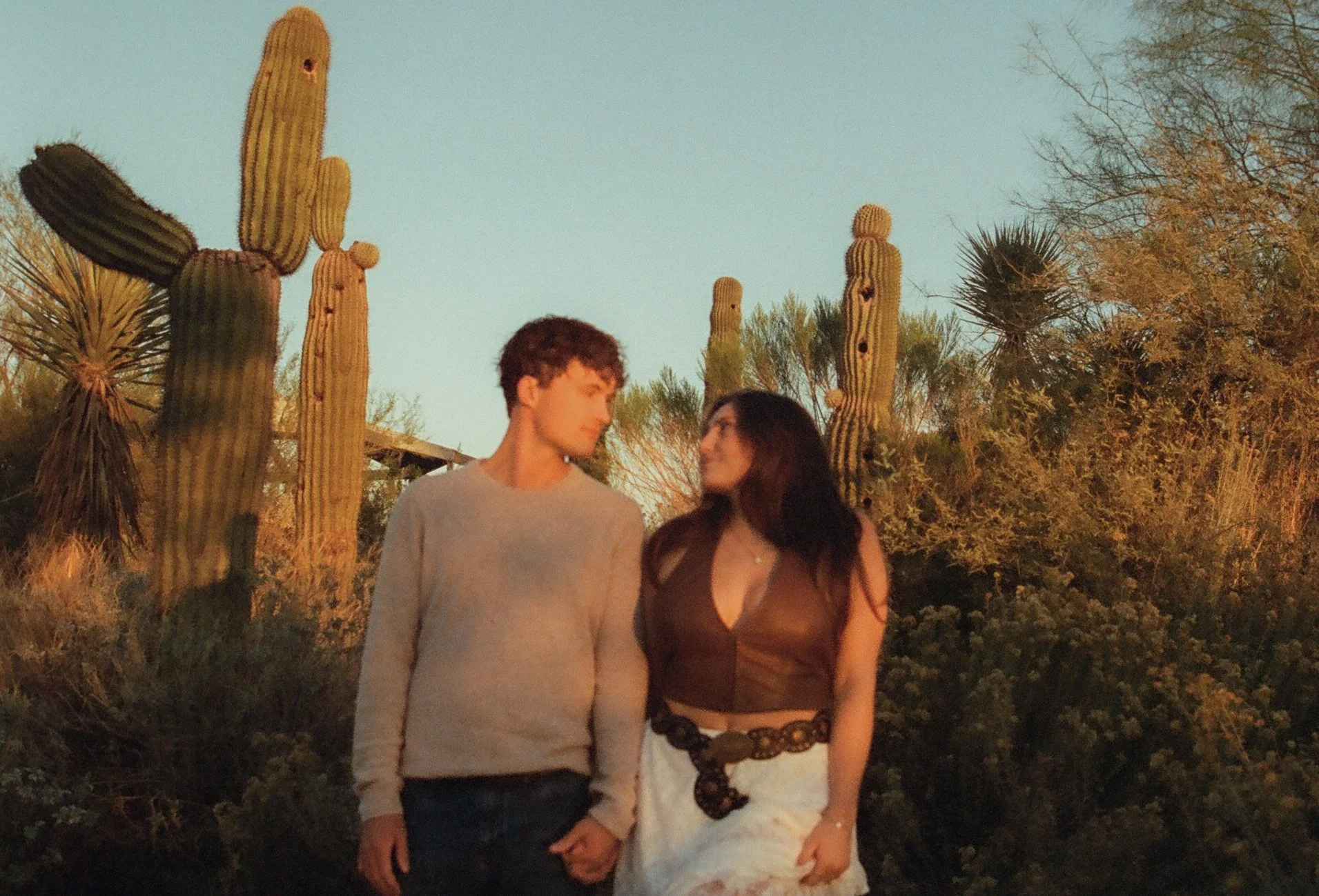 Couple walking hand-in-hand through golden desert light, surrounded by cacti and warm textures during a couple's photoshoot.