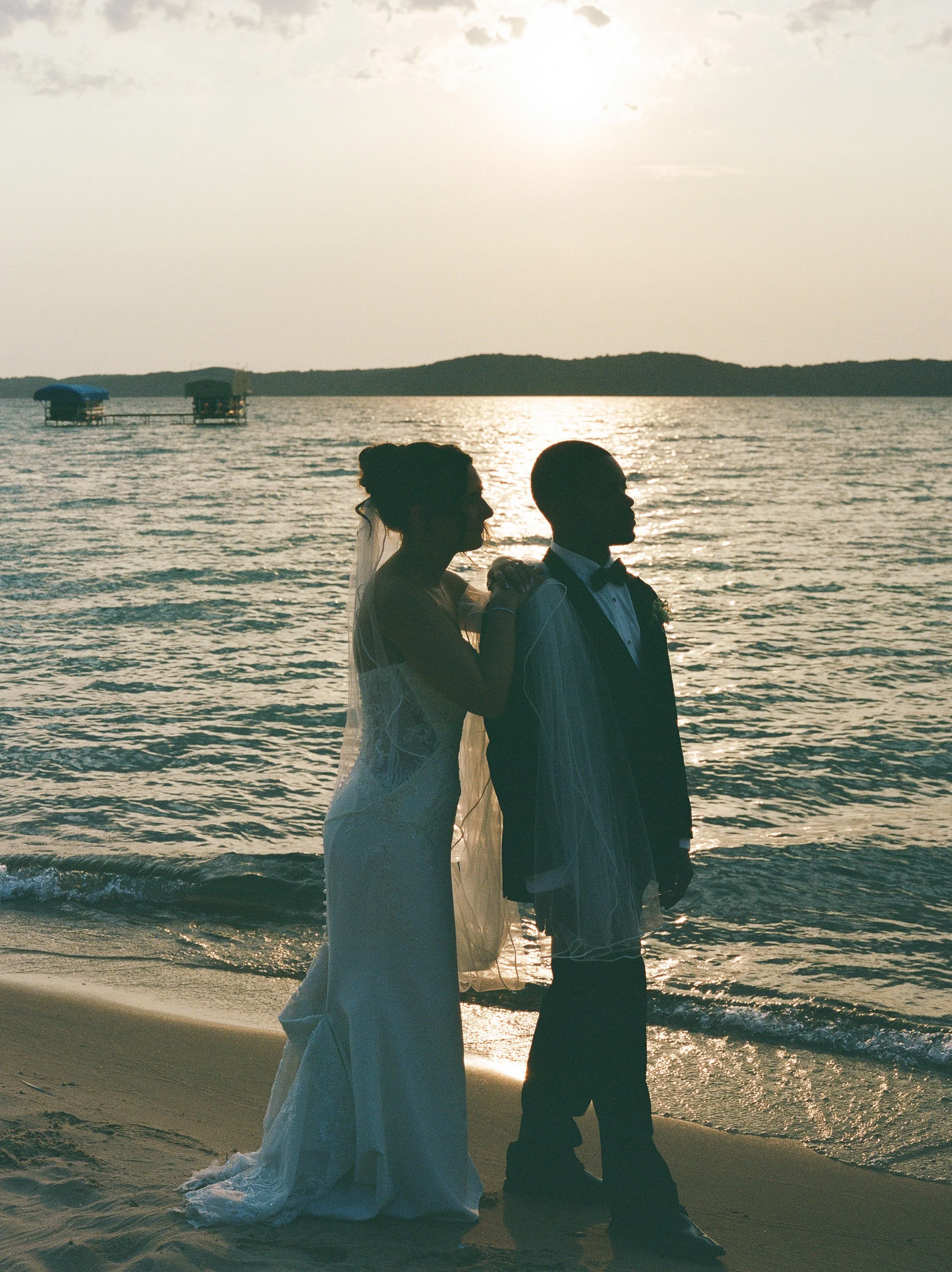 Bride and groom standing along the lakeshore at sunset during their Northern Michigan backyard wedding.
