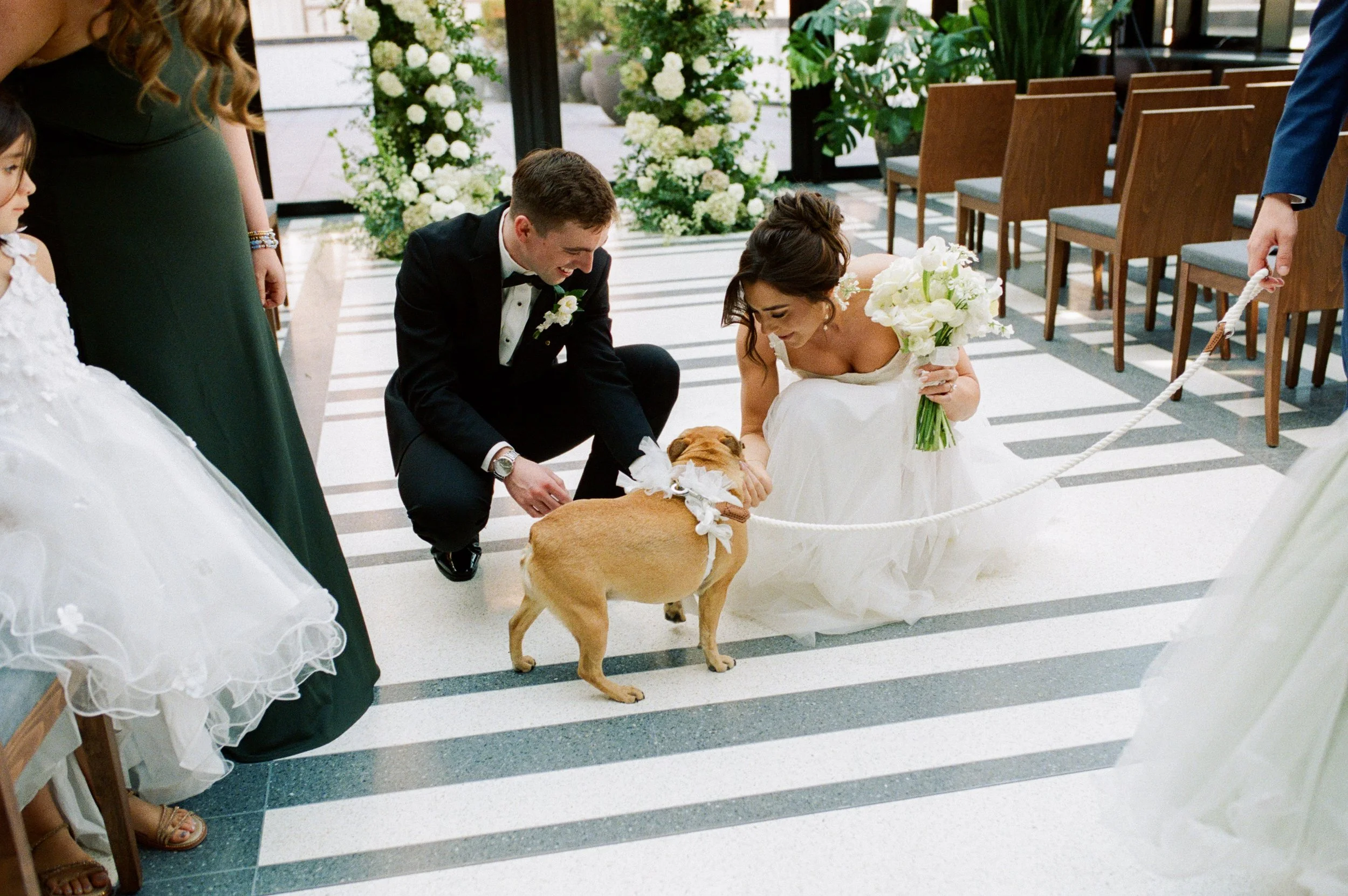 Newly married couple crouching down to pet their dog during their wedding ceremony