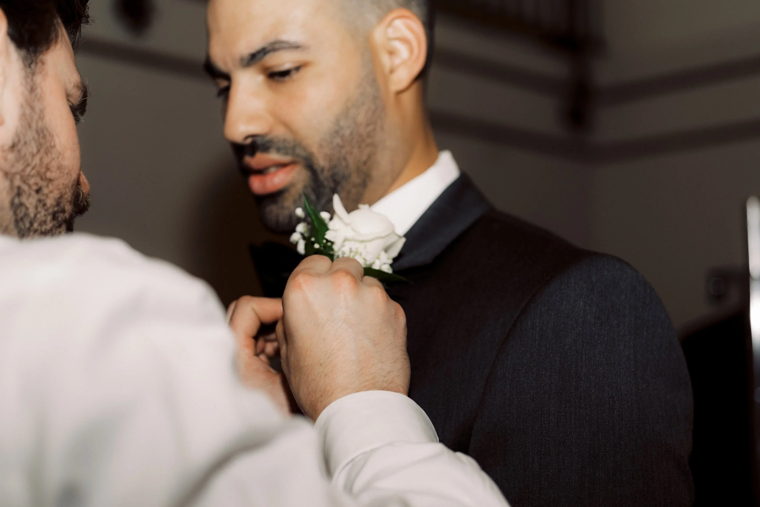 Close-up of a white rose boutonniere being pinned to the groom’s tuxedo before the downtown Detroit wedding.