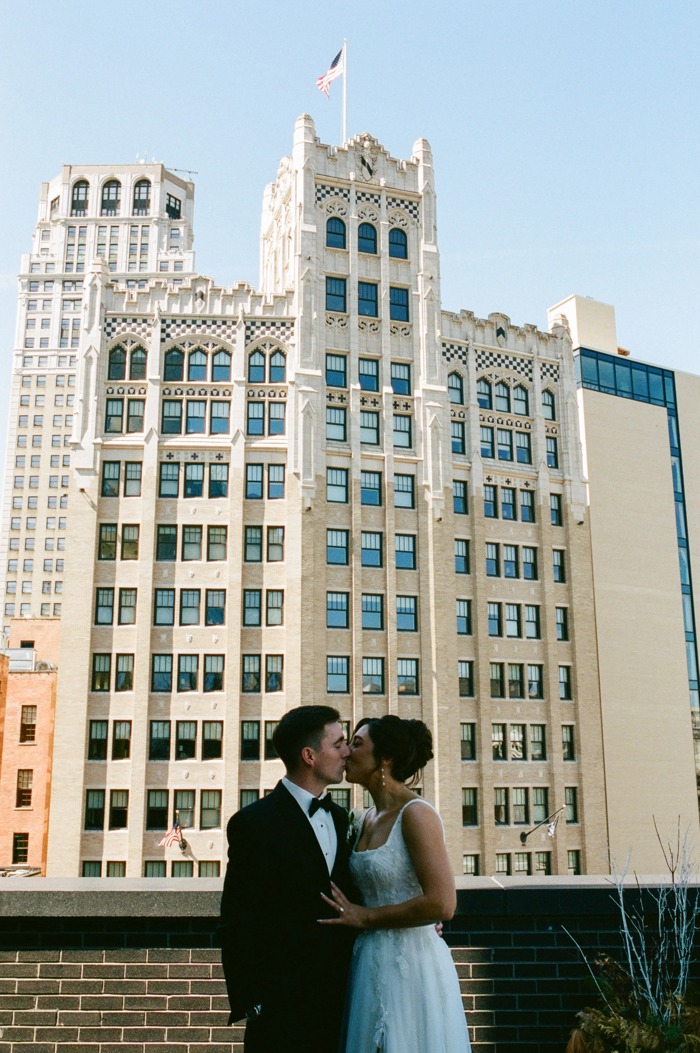 Bride and groom kissing on a rooftop with Detroit city buildings in the background during their Shinola Hotel wedding