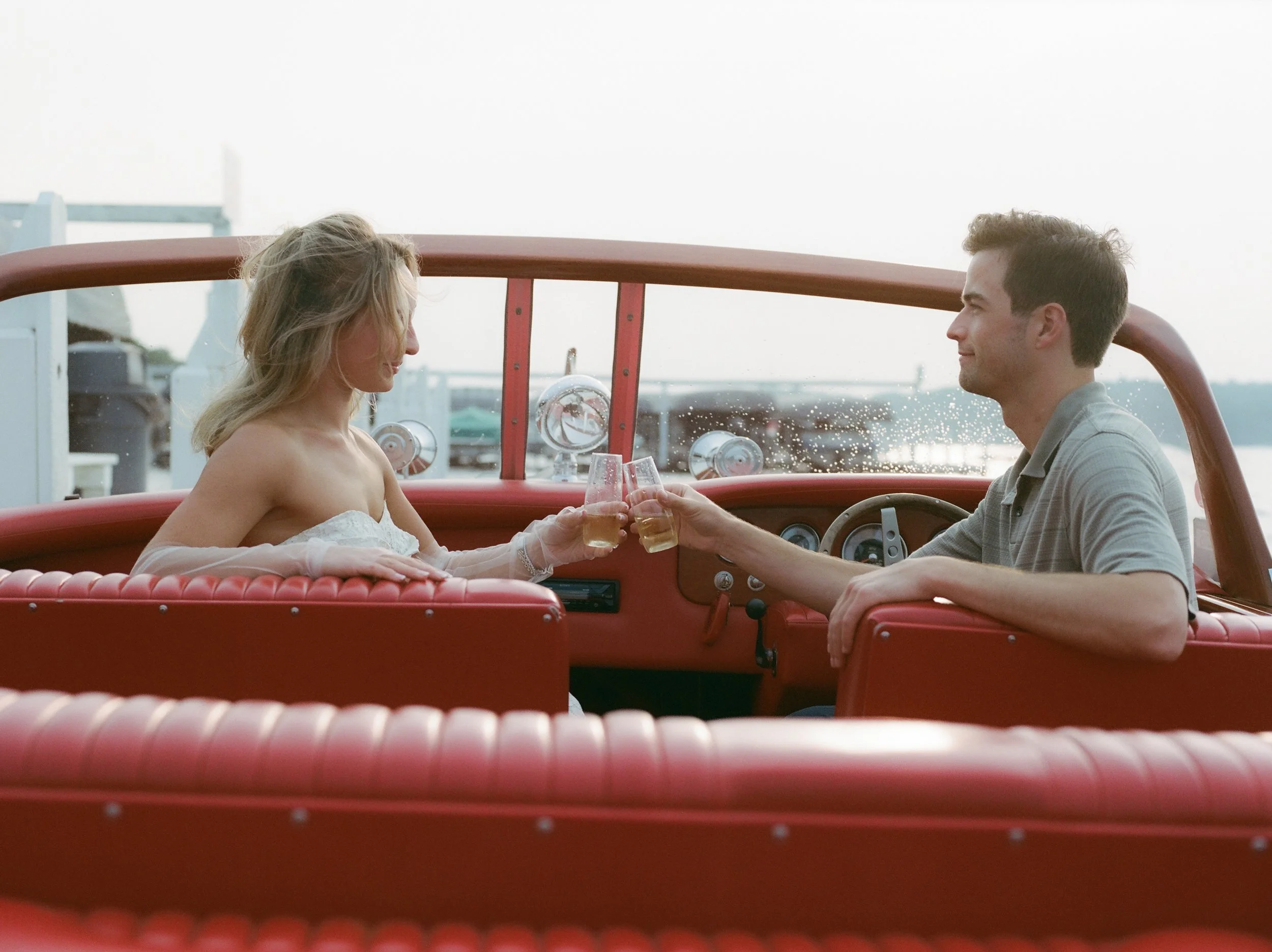 Couple toasting champagne glasses aboard a vintage wooden boat before sunset on the lake.