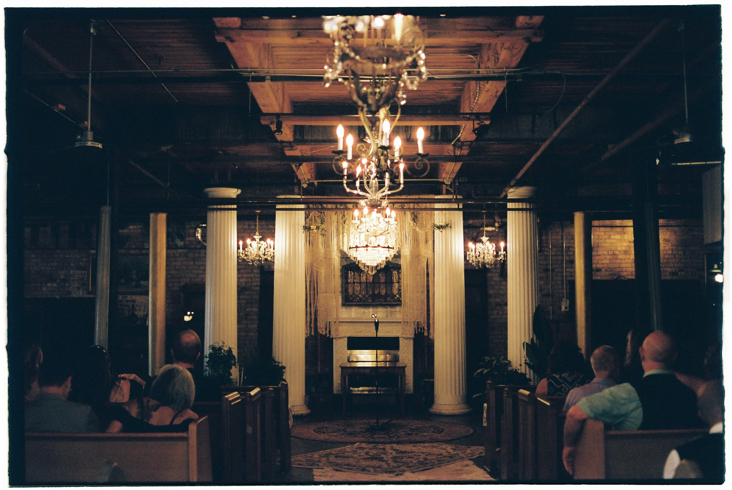 Moody candlelit ceremony space with chandeliers and columns set for a wedding at Salvage One