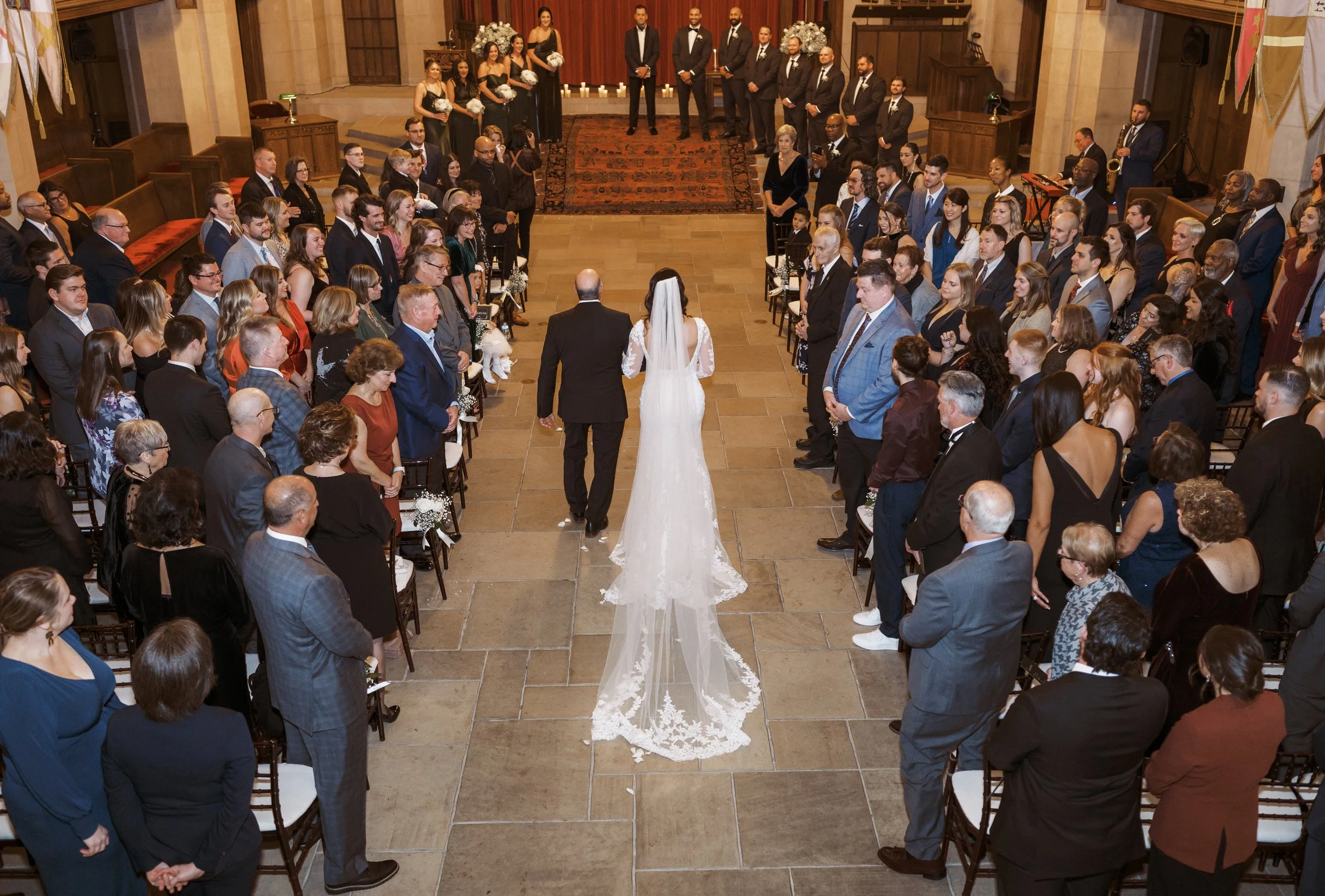 Bride walking down the ceremony aisle with her father as guests look on during the downtown Detroit wedding.