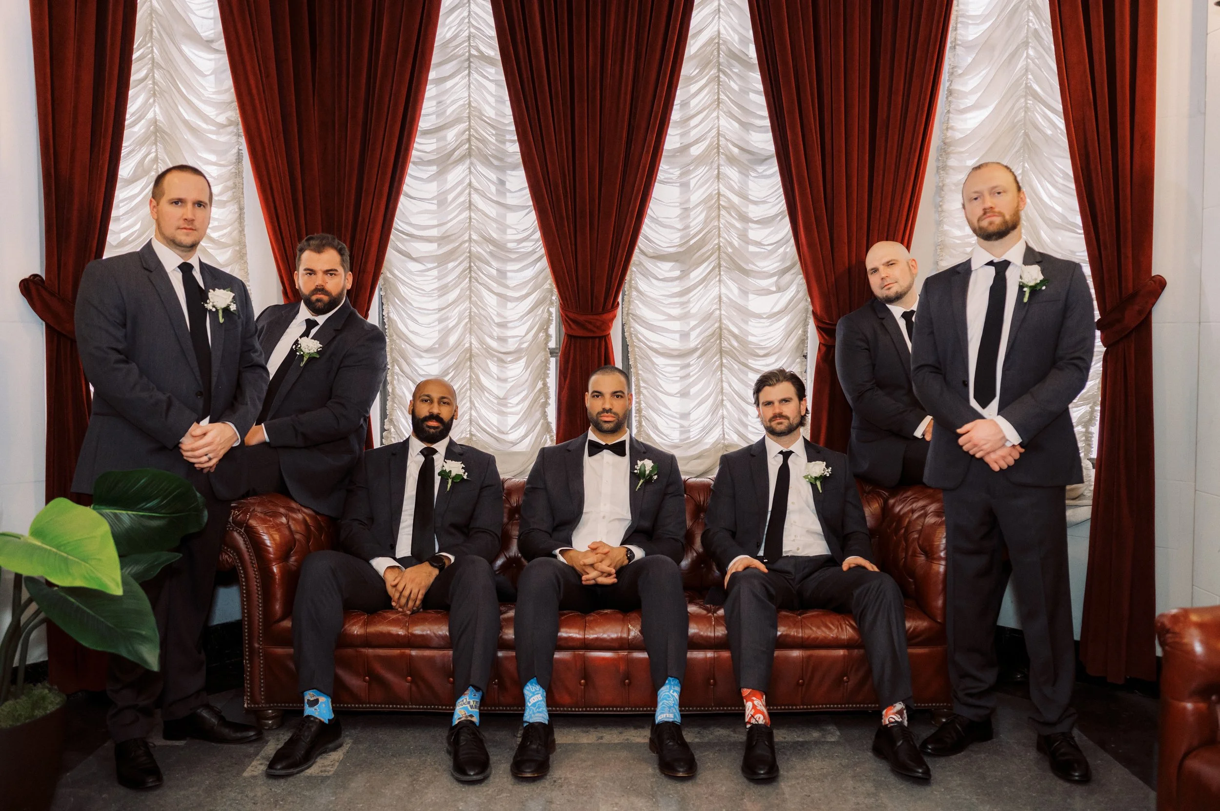 Groom and groomsmen posing together in black suits in front of dramatic red curtains during the downtown Detroit wedding.