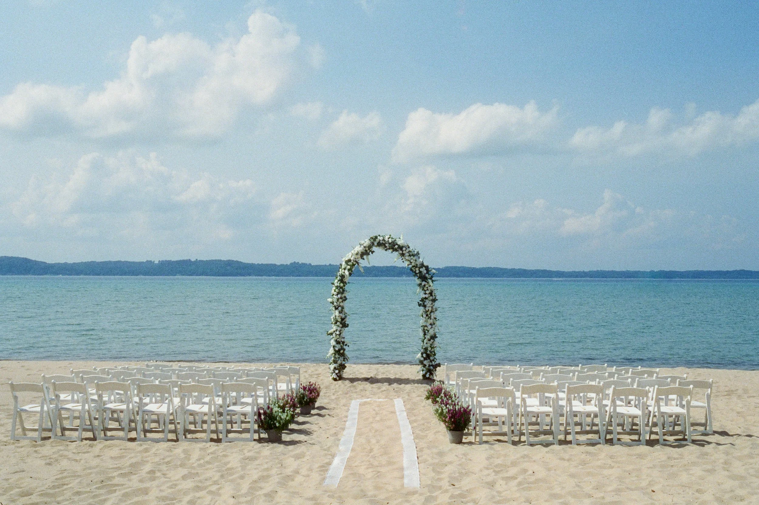 Lakeside wedding ceremony setup with white chairs, colorful potted flowers, and a floral arch at a Northern Michigan backyard wedding.