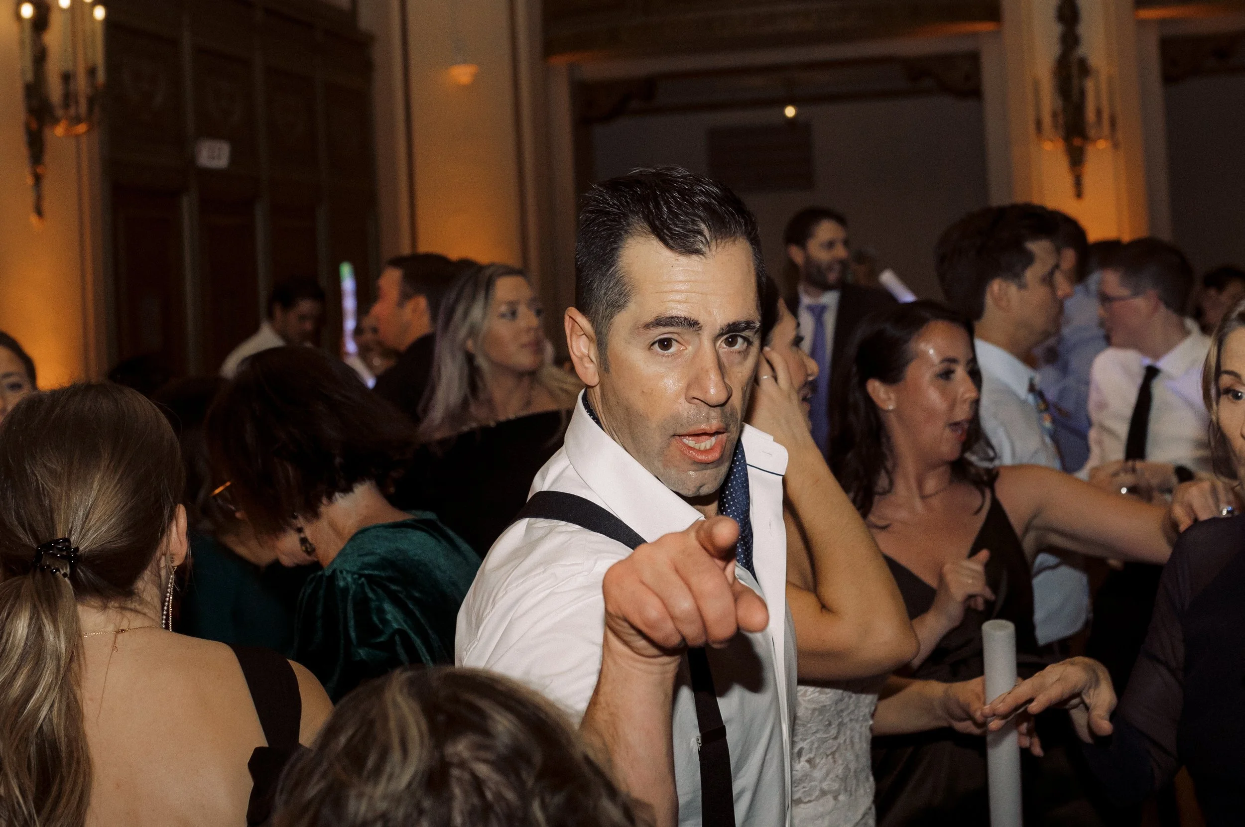 A wedding guest dances on the dance floor while pointing at the camera