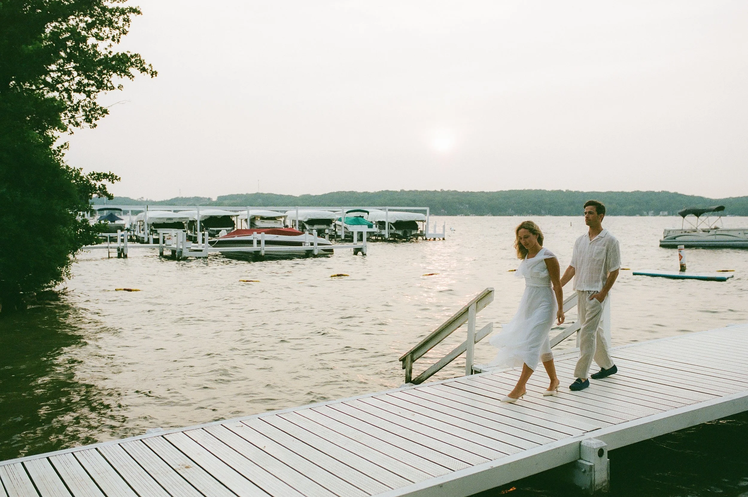 Couple walking hand in hand along a lakeside dock during a relaxed Lake Geneva Engagement session at golden hour.