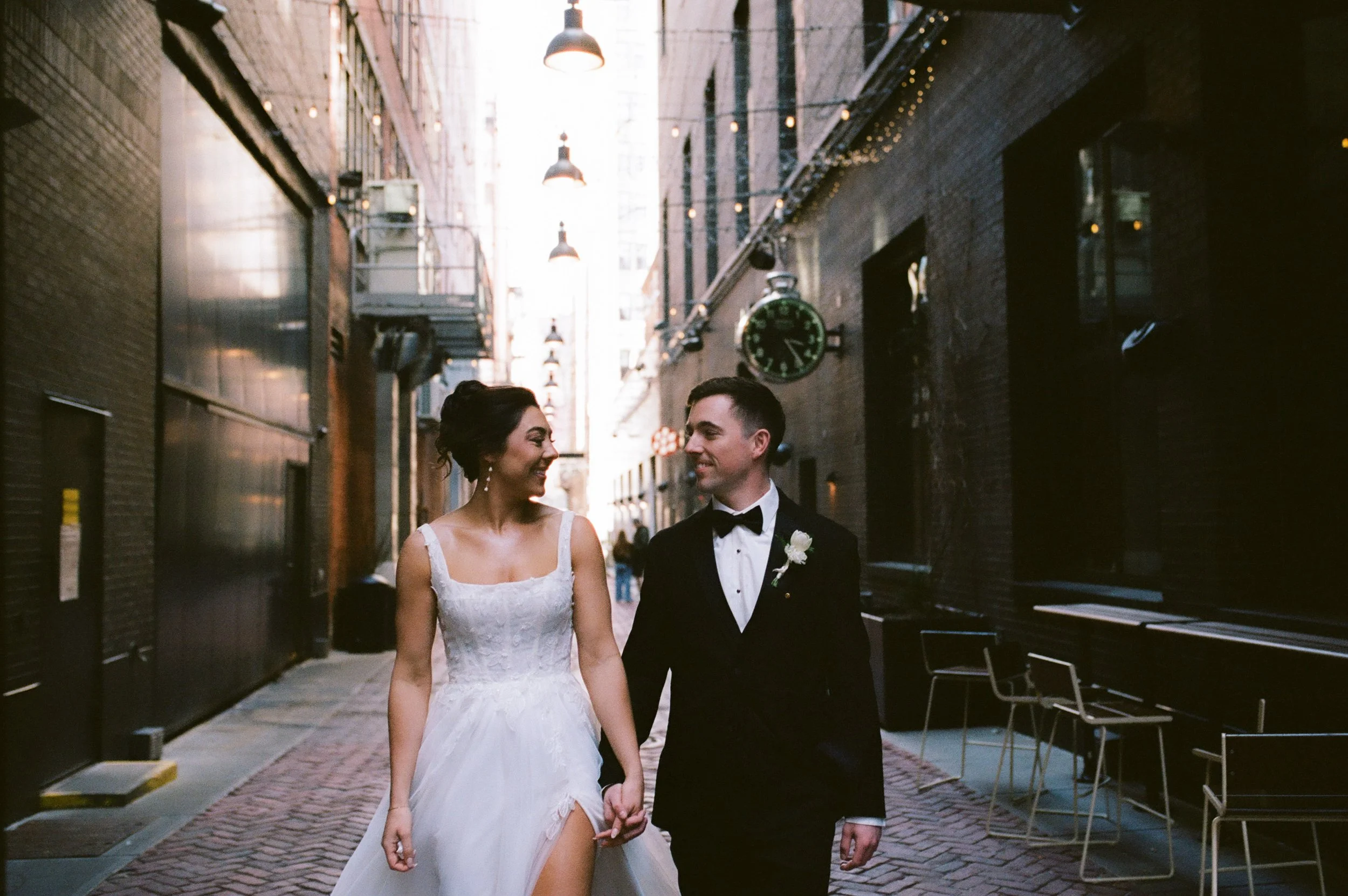 Bride and groom walking through a Detroit alleyway in formal wedding attire during golden hour portraits