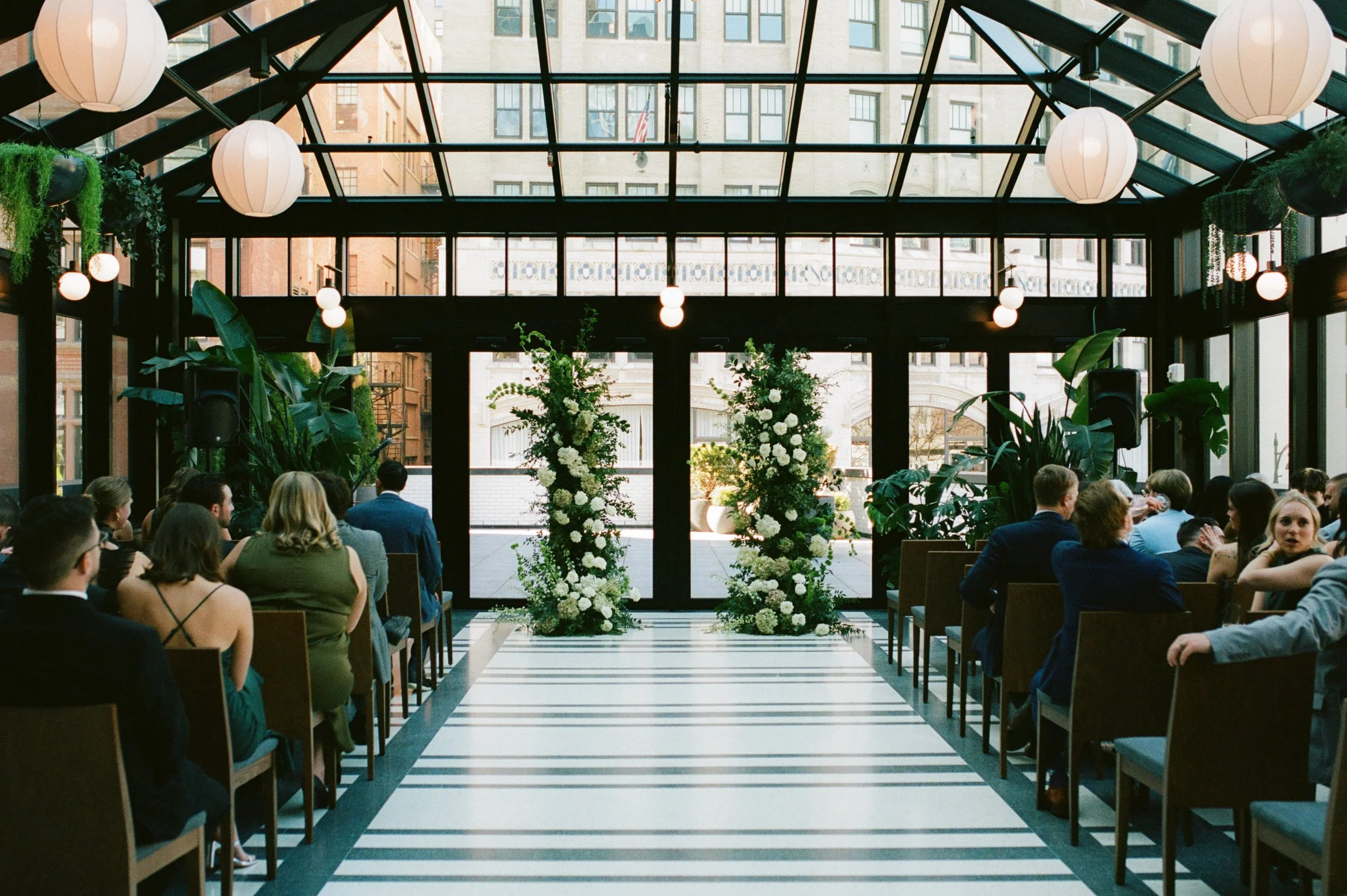 Ceremony setup with guests seated beneath the glass atrium and floral pillars at Shinola Hotel in Detroit