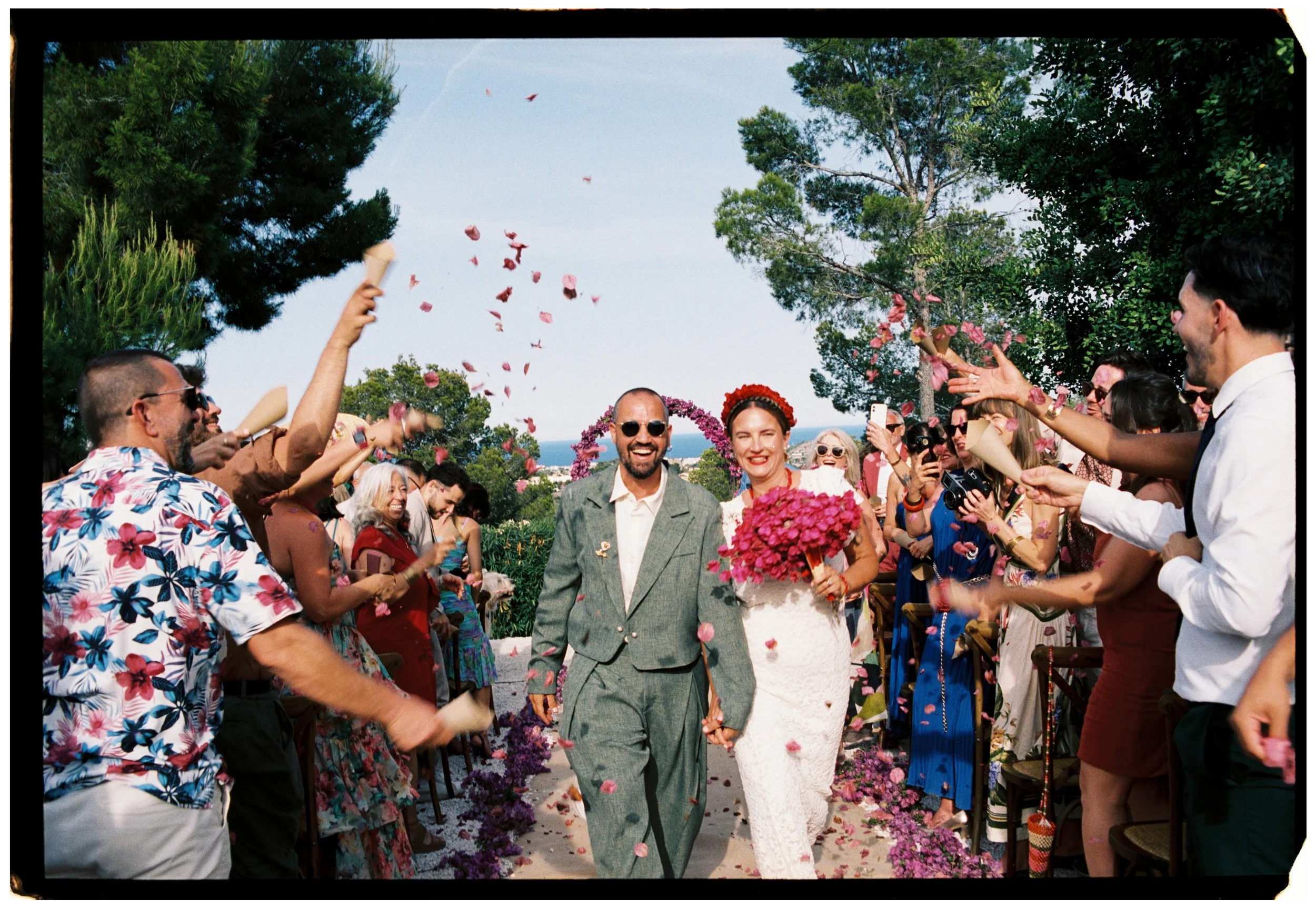 Newlyweds walking through a shower of pink flower petals after their Spain wedding ceremony.