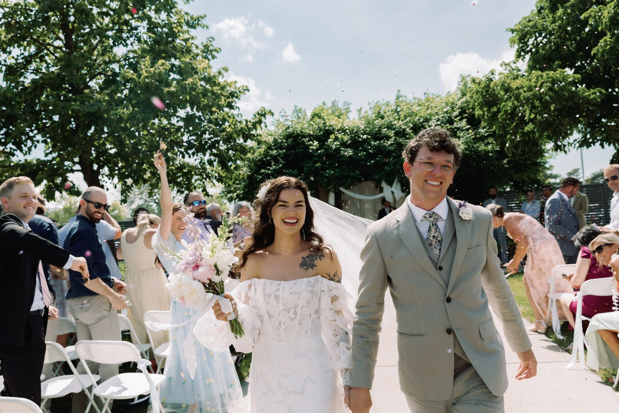 Bride and groom walking down the aisle just married, smiling as guests toss confetti in celebration